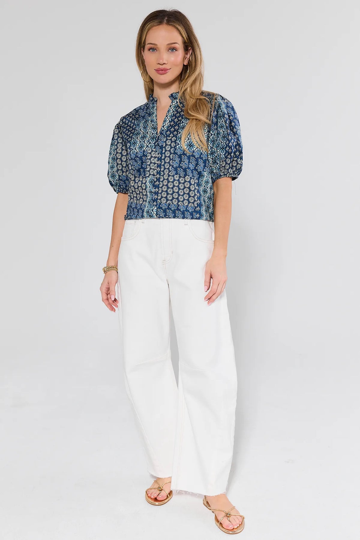 Woman wearing a blue patterned blouse and white pants on a light gray background