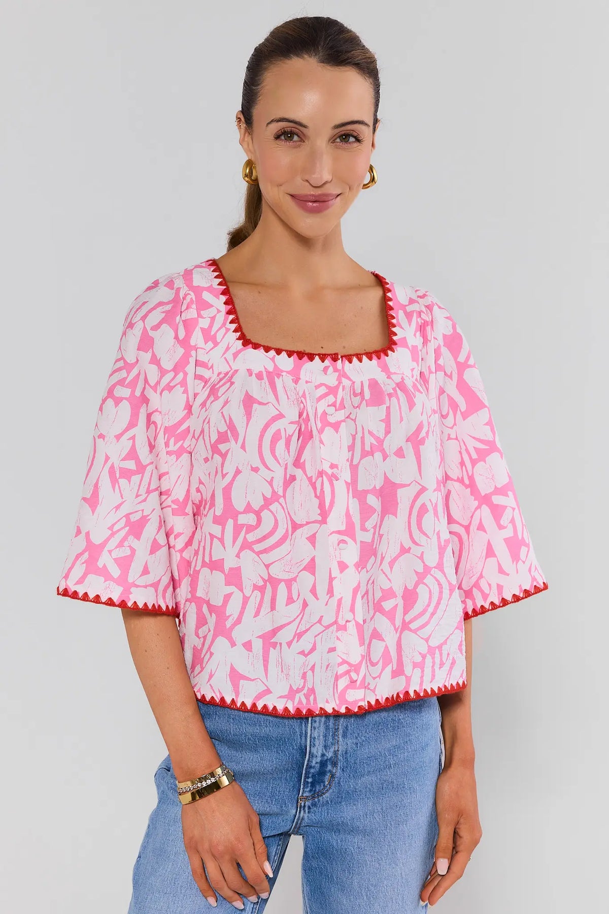 Woman wearing a pink and white patterned blouse with blue jeans on a plain background