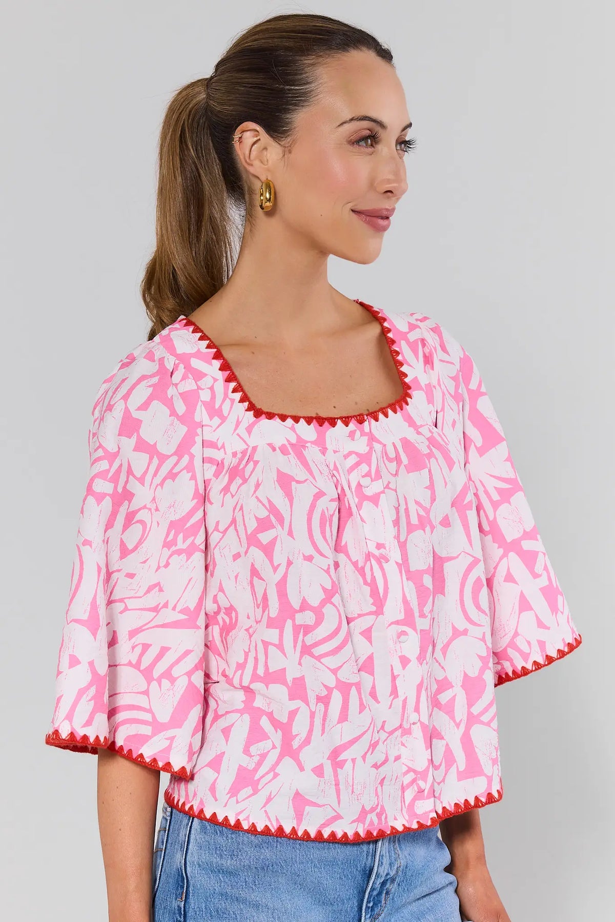 side shot Woman wearing a pink and white patterned blouse with blue jeans on a gray background