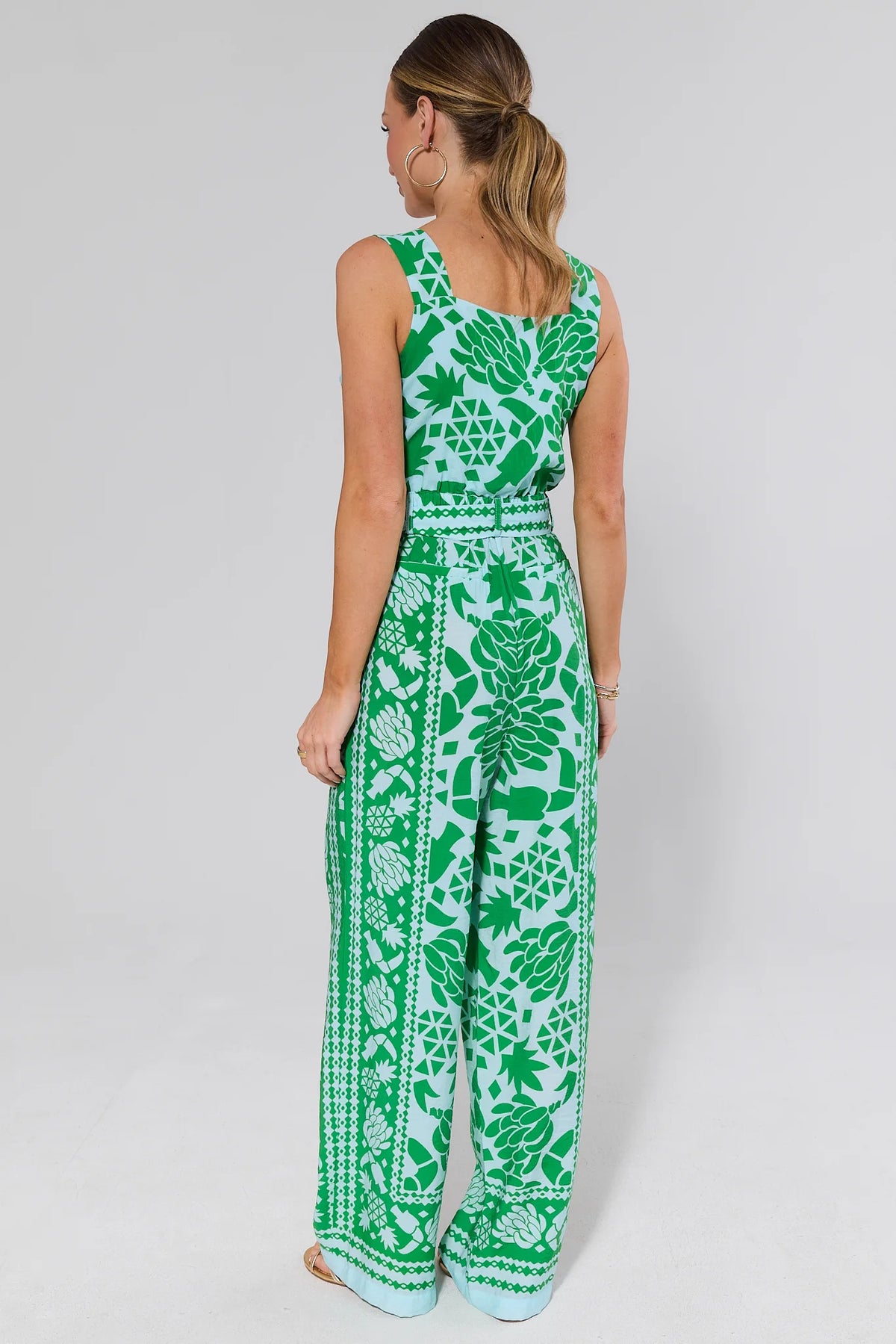 Woman standing wearing a green and white patterned jumpsuit on a plain background