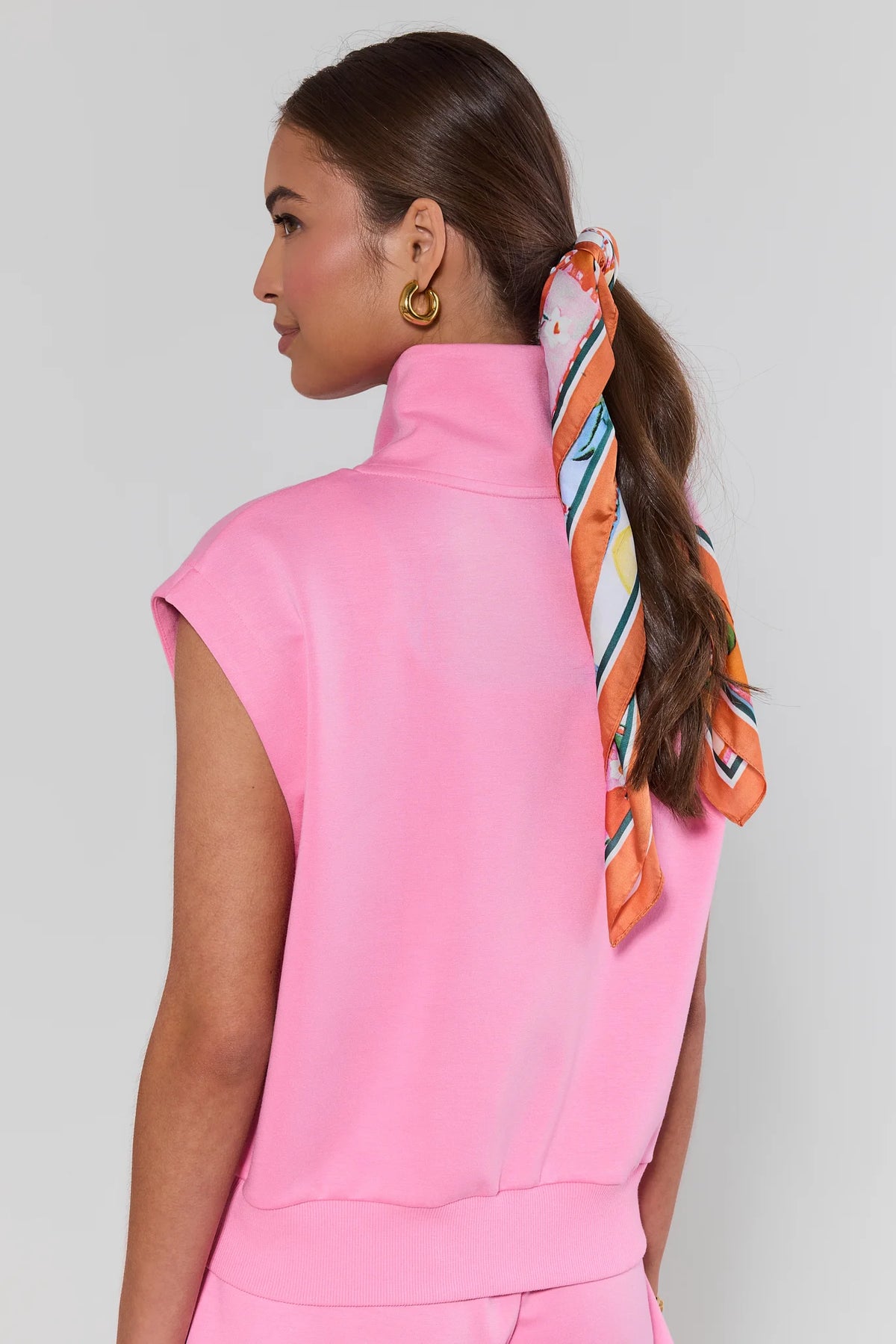 Woman wearing a pink outfit with a colorful scarf tied in her hair against a gray background