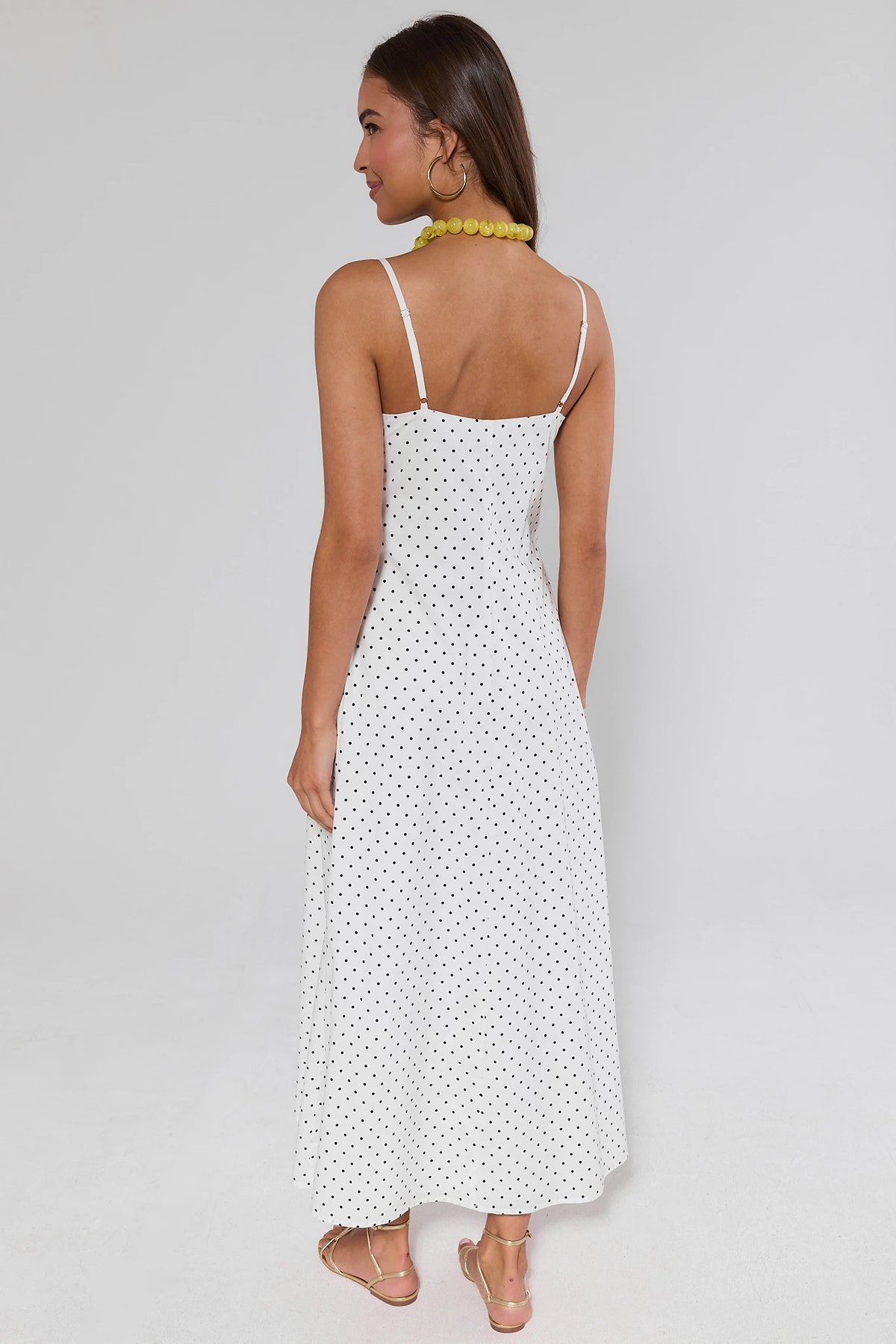 Woman standing wearing a white polka dot dress on a gray background