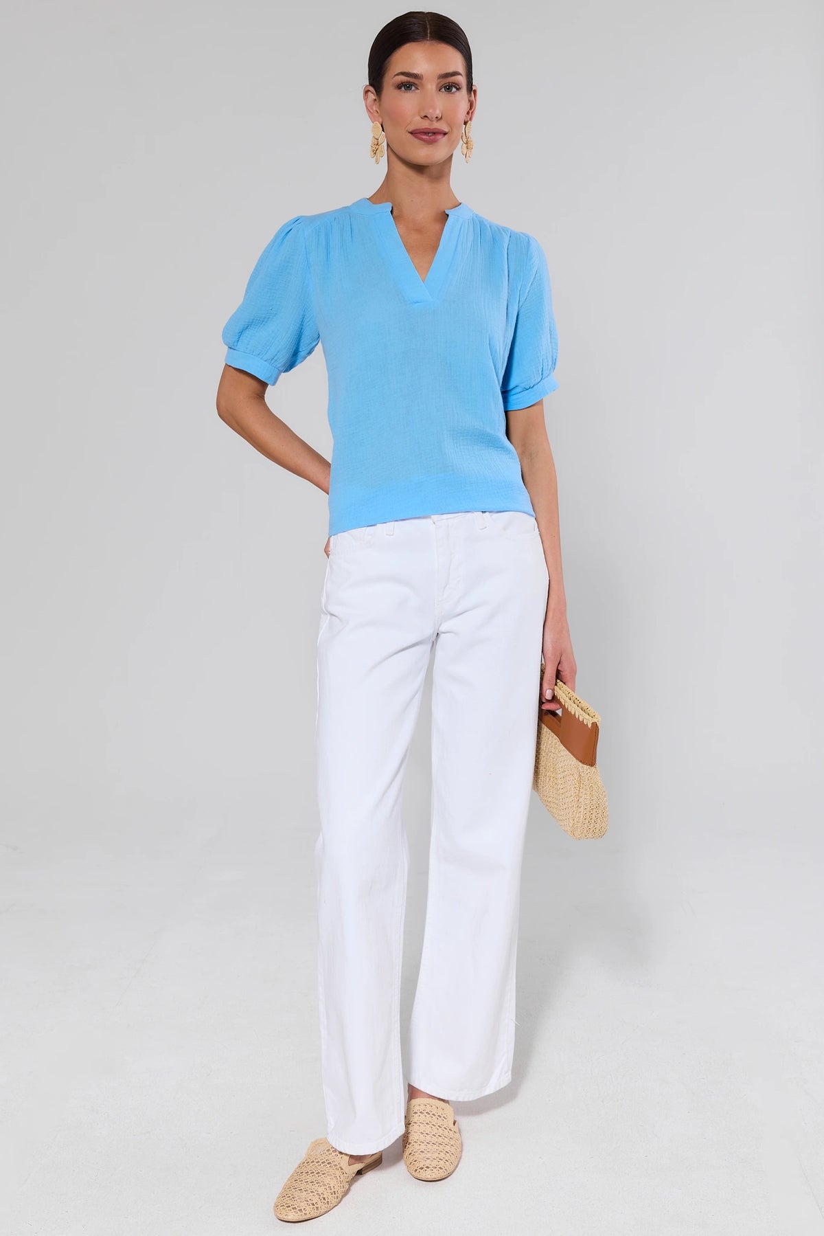 Woman wearing light blue gauze top with white wide-leg pants and woven mules, full-length front view | Avara