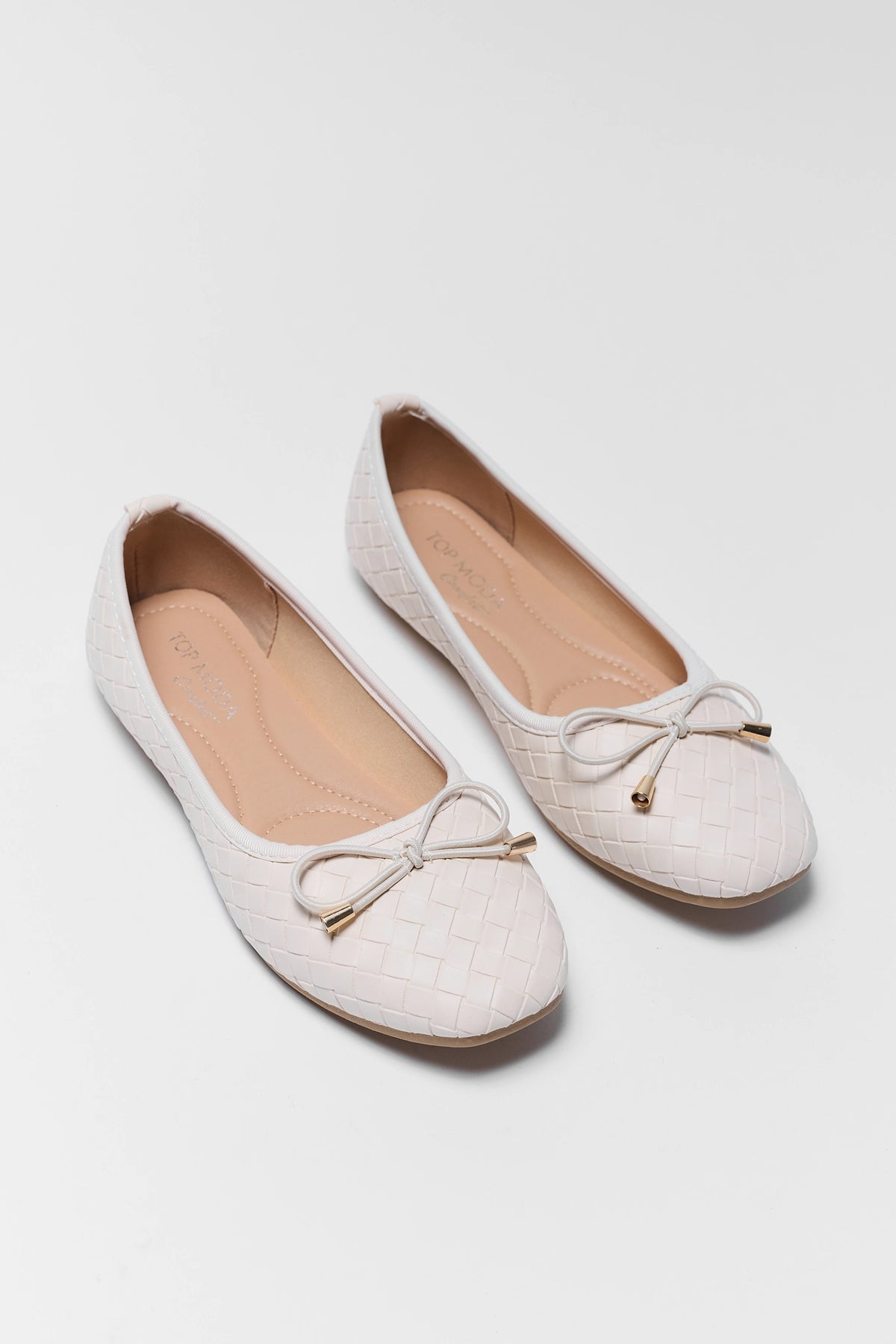 Pair of white woven flats with gold-tipped bow, angled view showing insole | Avara