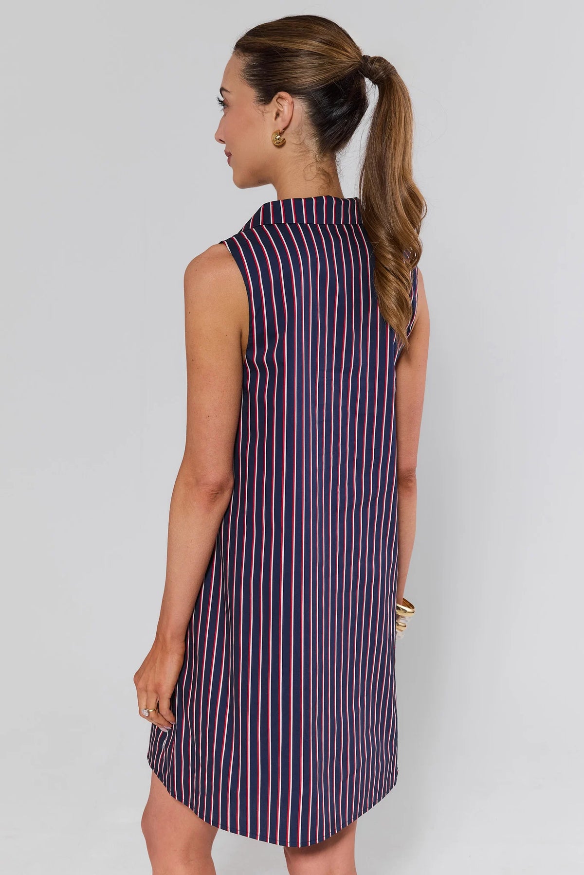 Woman standing wearing a sleeveless striped dress against a plain background