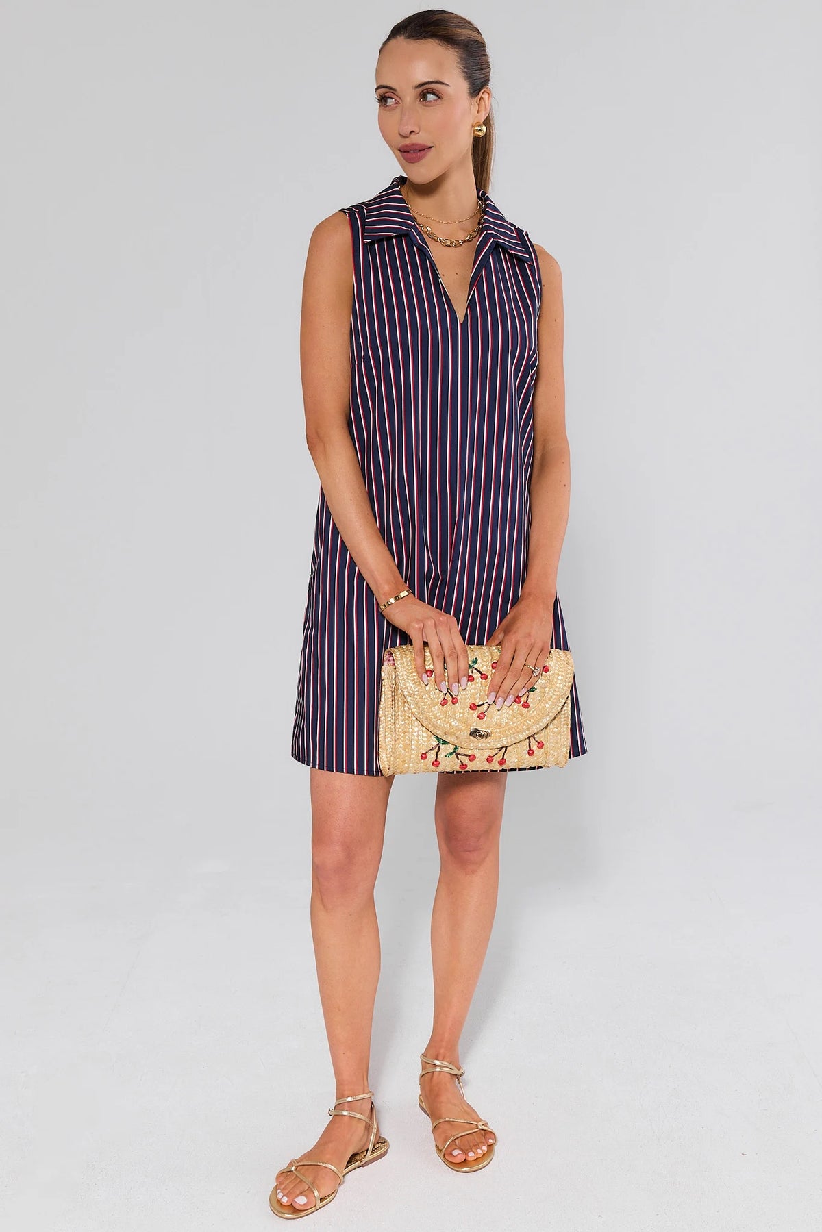 Woman wearing a striped dress holding a clutch against a white background