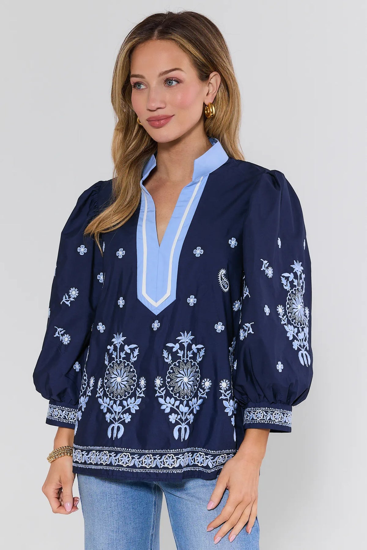 Woman wearing a navy blue blouse with white embroidery on a plain background