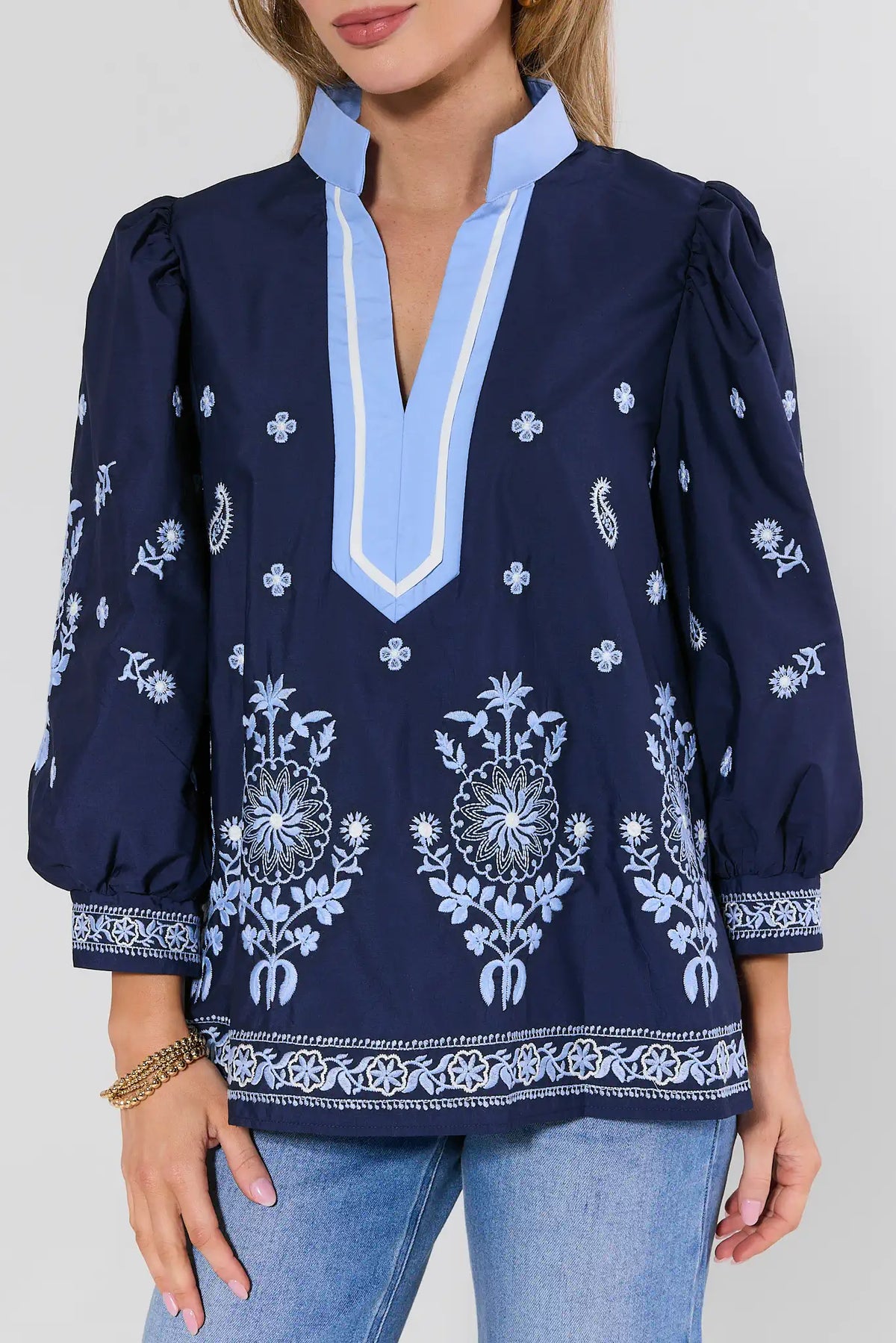 Navy blue blouse with white embroidery and light blue trim worn by a person on a plain background