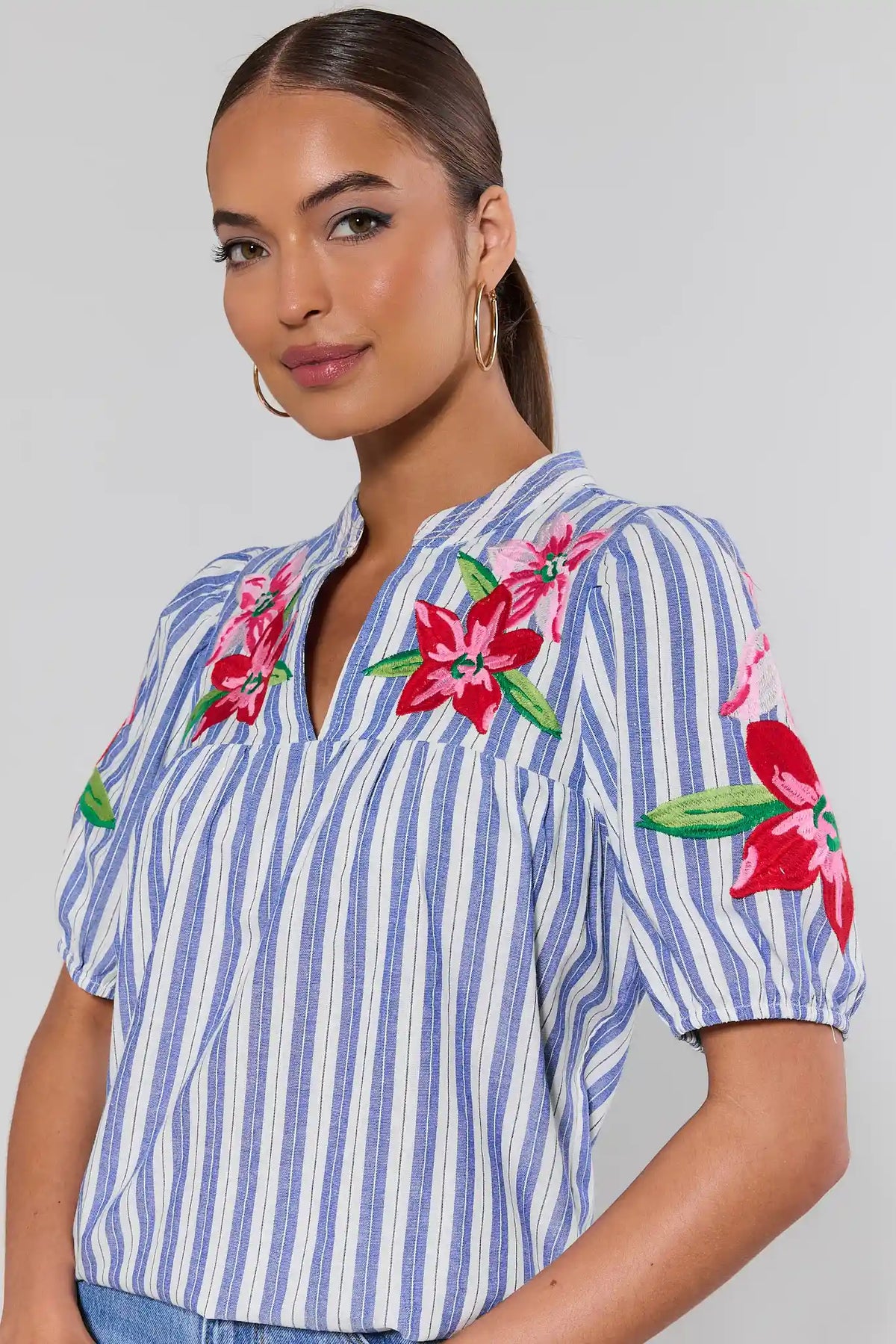close up Woman wearing a blue and white striped shirt with floral embroidery on a gray background