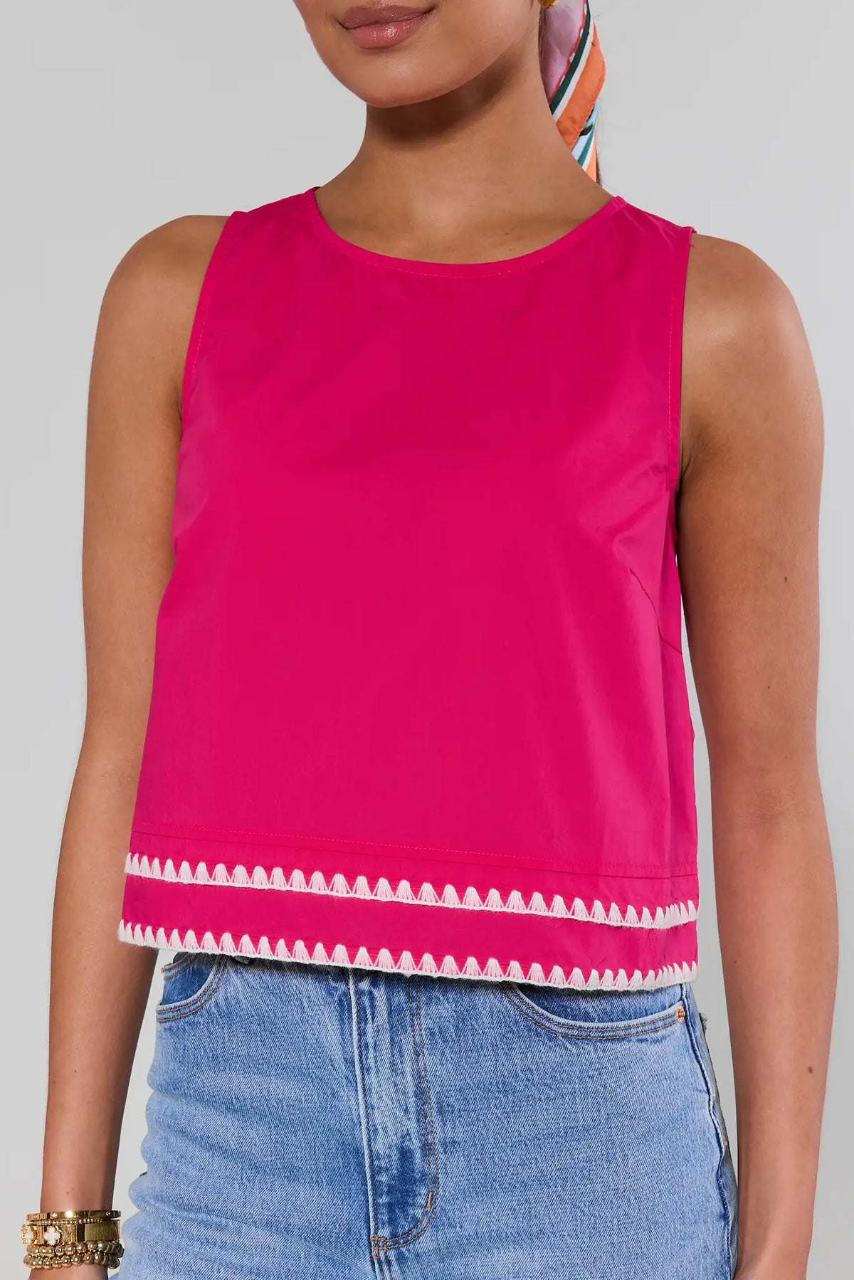 close up Person wearing a bright pink sleeveless top with white trim and blue jeans on a gray background