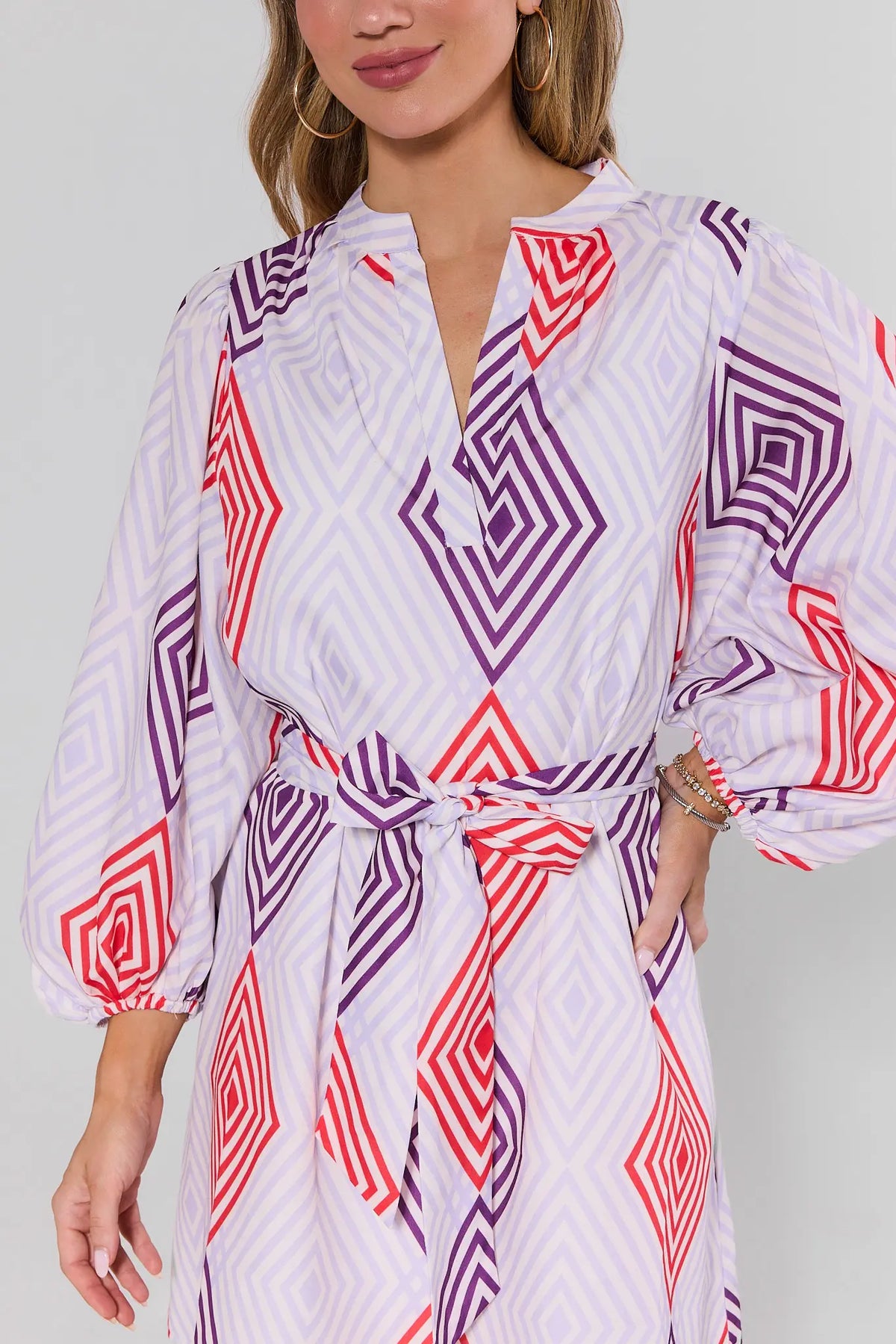 close up Woman wearing a white dress with red and purple geometric patterns on a plain background