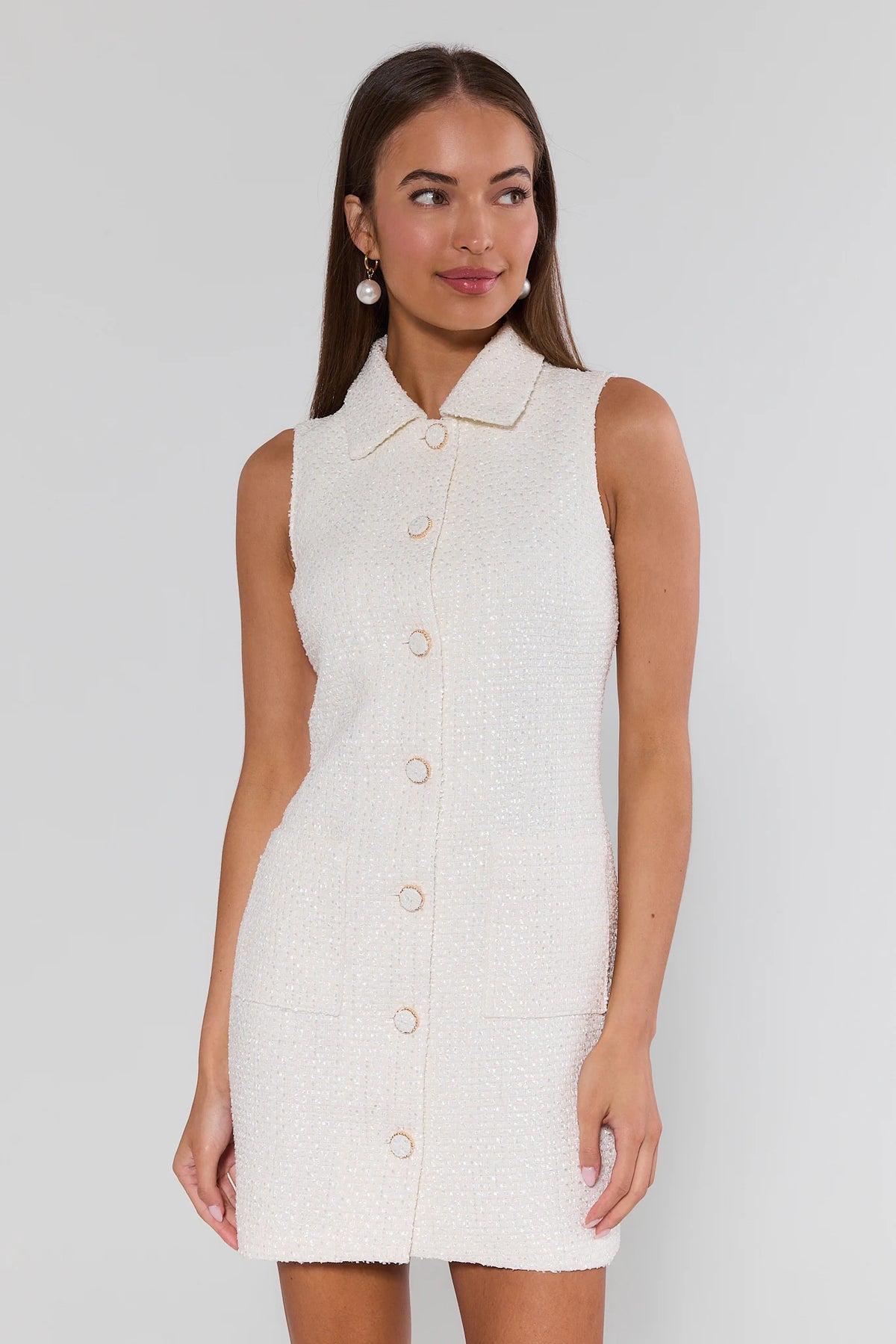 Woman wearing a white sleeveless dress with buttons on a plain background