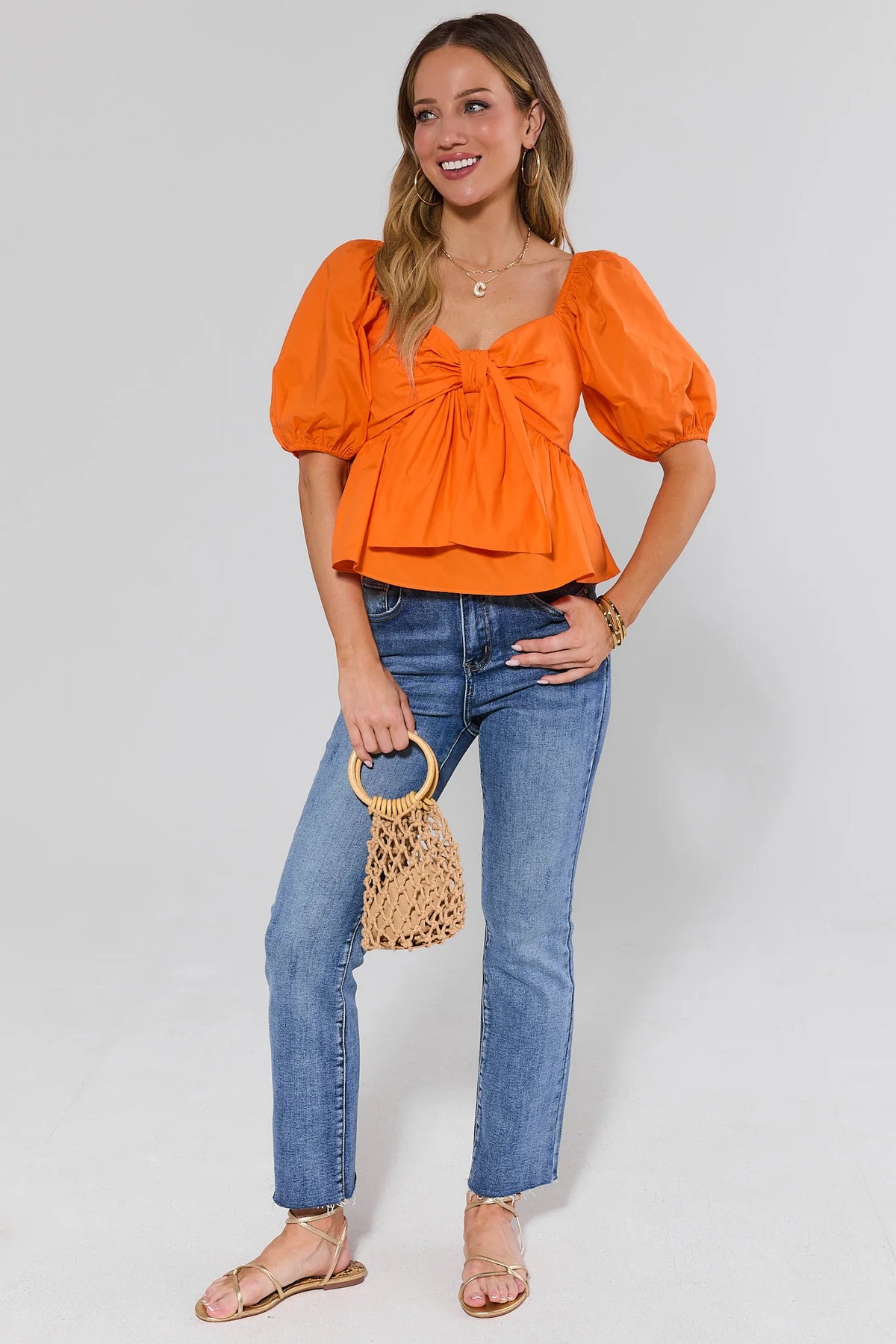 Orange puff sleeve peplum top styled with blue jeans and woven bag - Full Length Front View | Avara