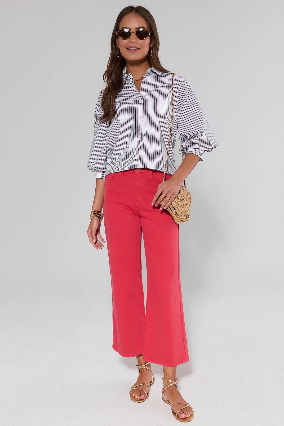 Woman wearing a striped shirt and red pants with sunglasses and a clutch on a white background