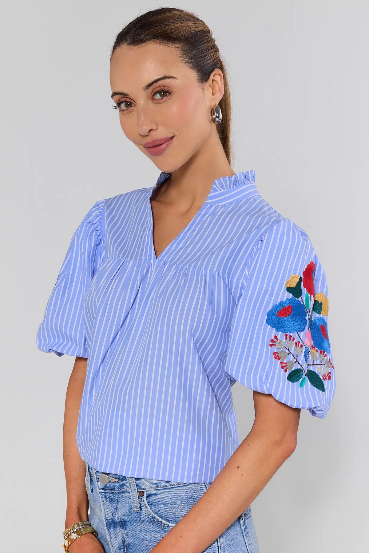 Woman wearing a blue striped blouse with floral embroidery on a plain background