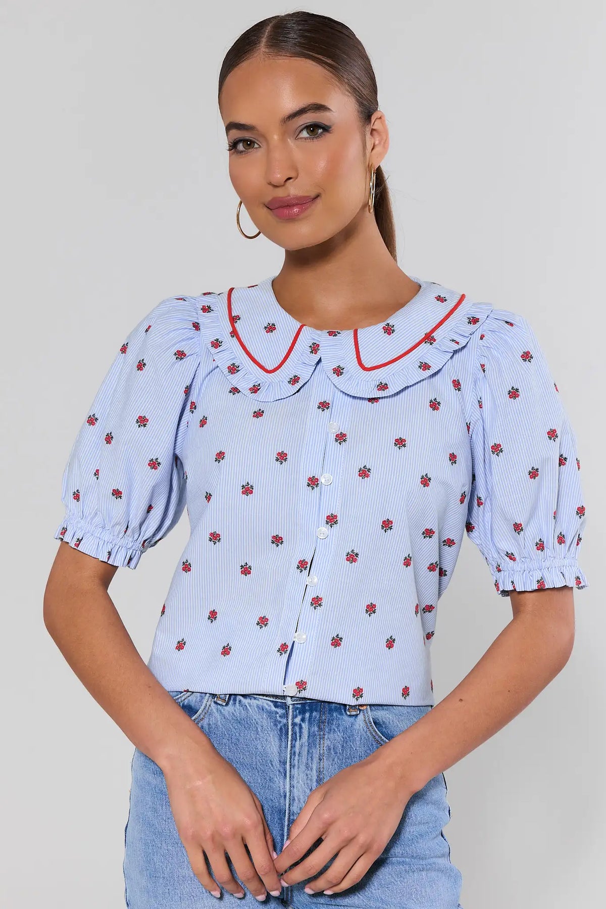 Woman wearing a light blue blouse with red floral pattern and red collar against a plain background