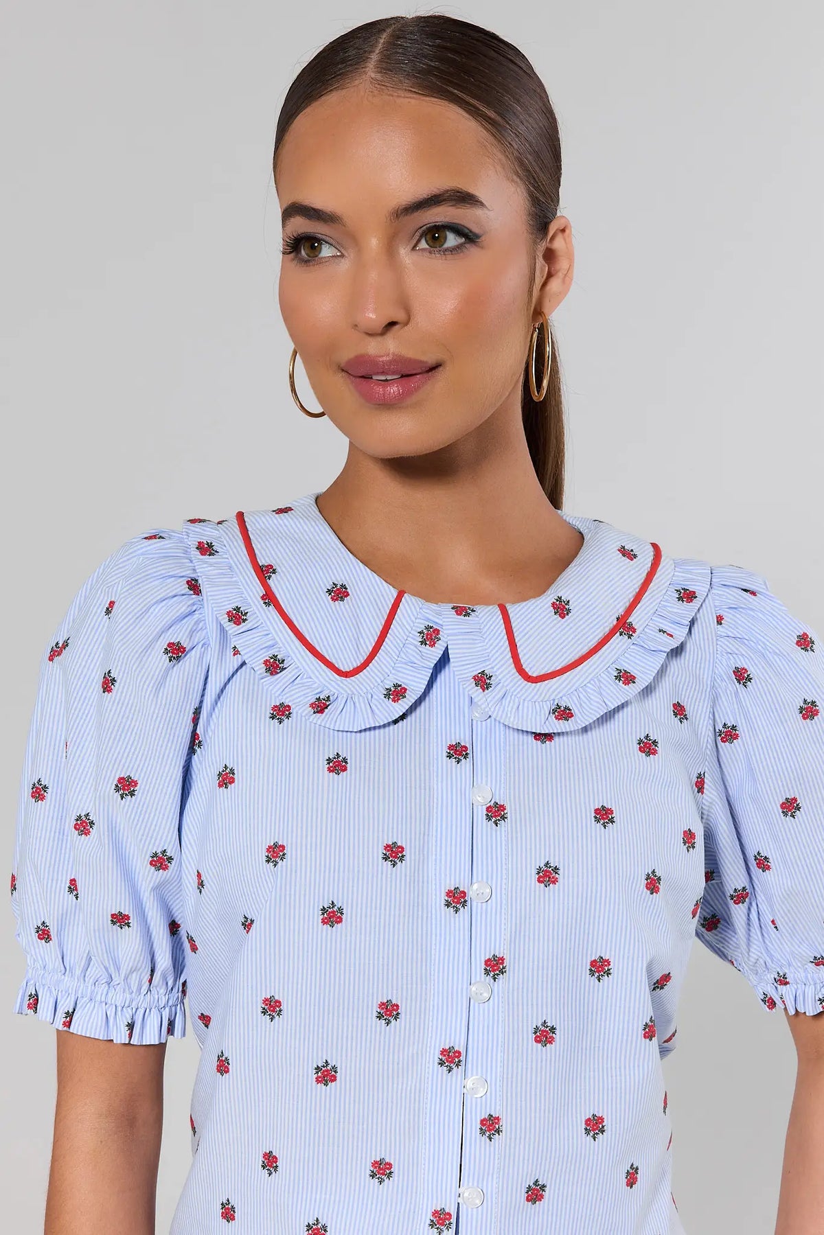 close up Woman wearing a light blue blouse with floral pattern and red trim on a plain background