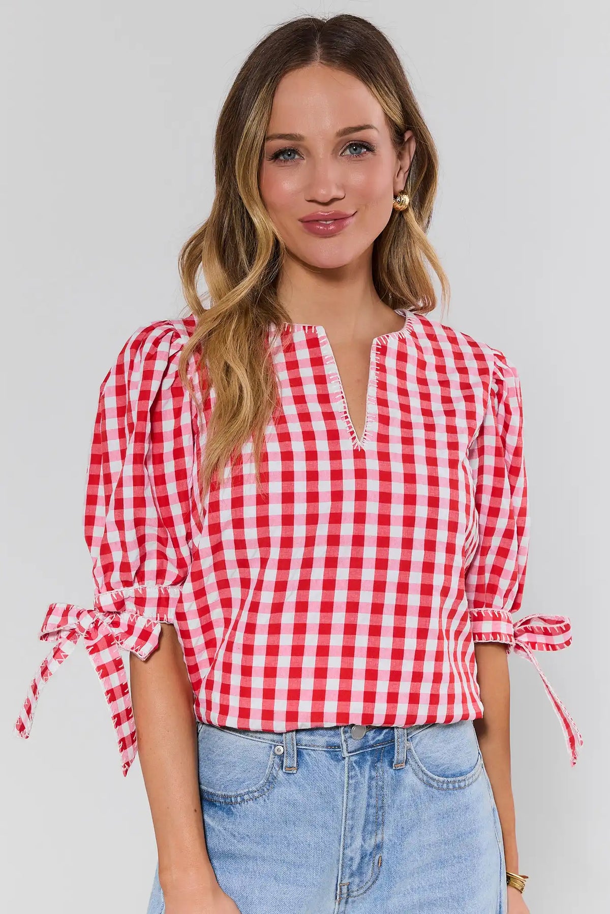 Women's red gingham puff sleeve blouse with tie sleeves, styled with light wash jeans - Front View | Avara