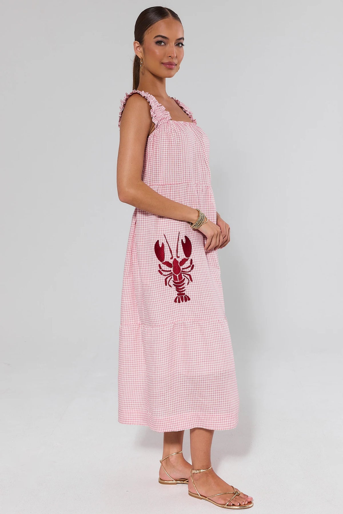 Red gingham lobster midi dress side profile showing tiered skirt, lobster embroidery, and gold sandals | Avara