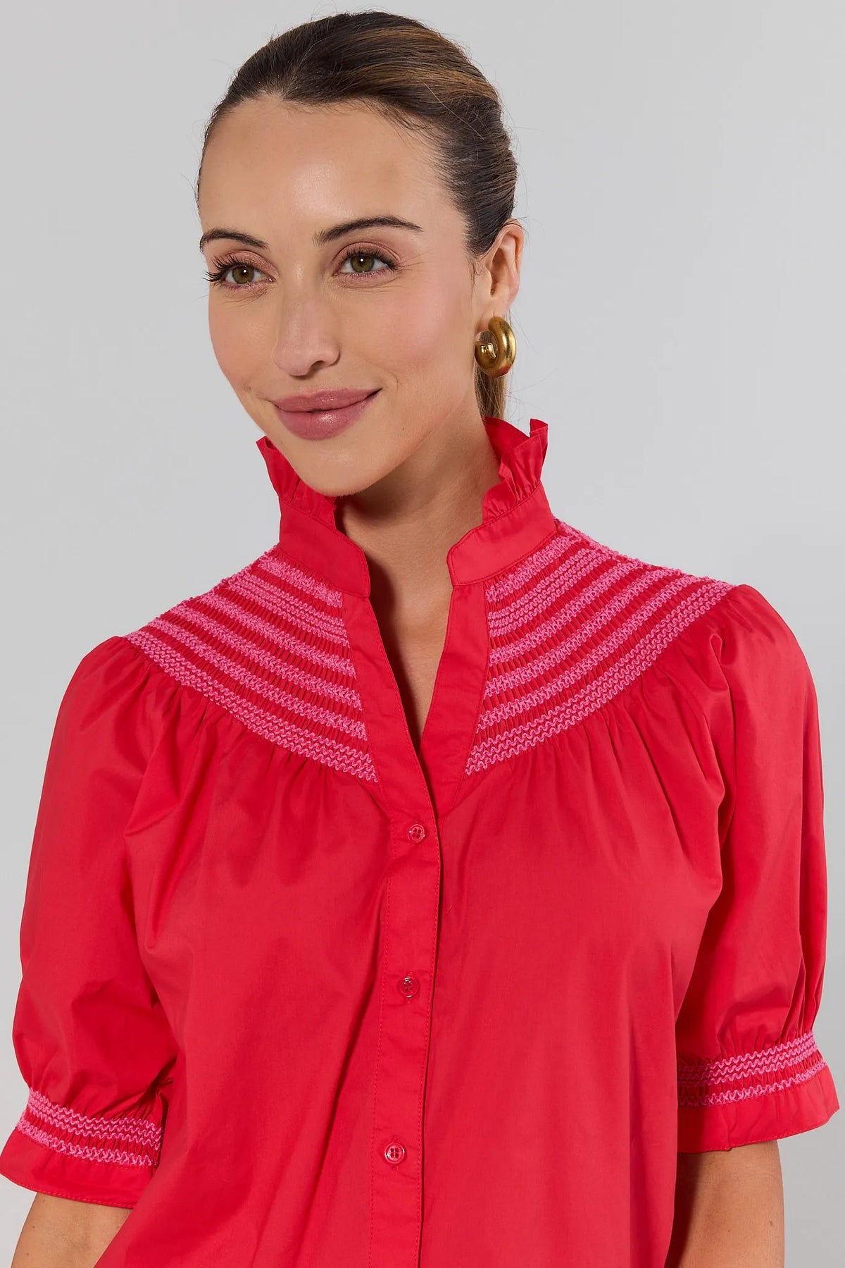 Close-up of pink embroidery detail on red button-up top with ruffle neckline and puff sleeves | Avara
