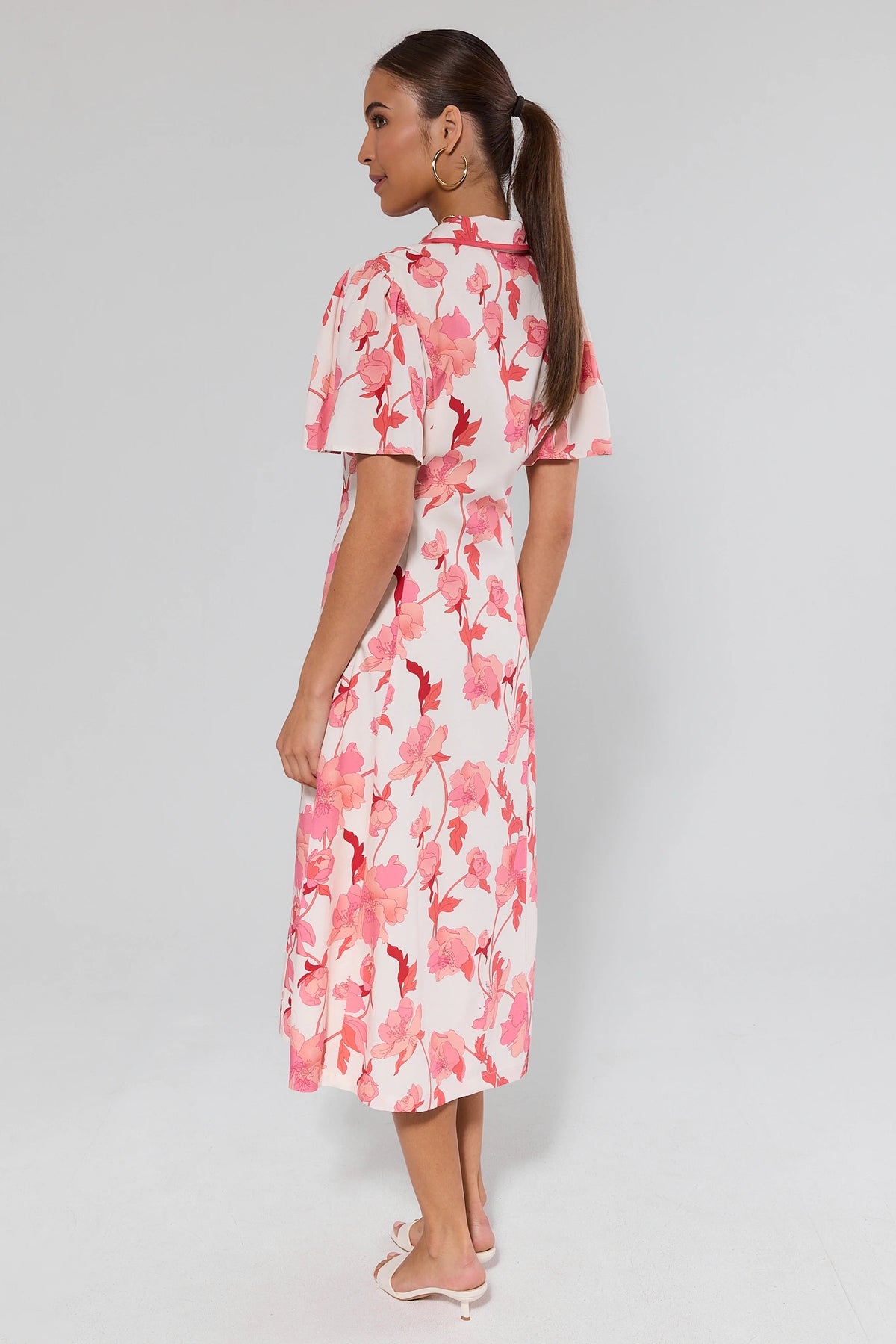 Woman wearing a pink floral modest midi dress with A-line silhouette and flutter sleeves - Back View | Avara