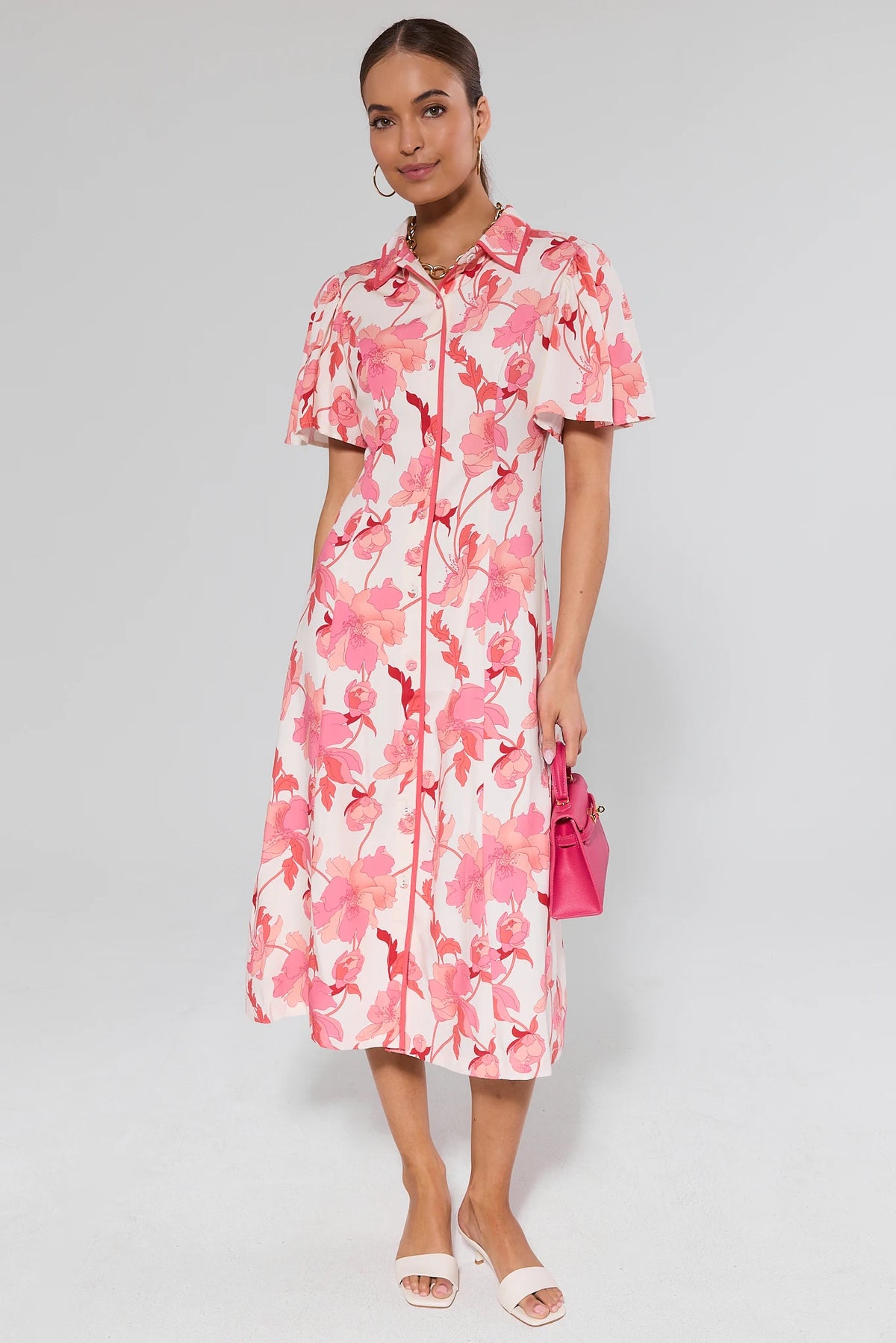 Woman wearing a pink floral button-up midi dress with flutter sleeves, holding a pink bag - Front View | Avara