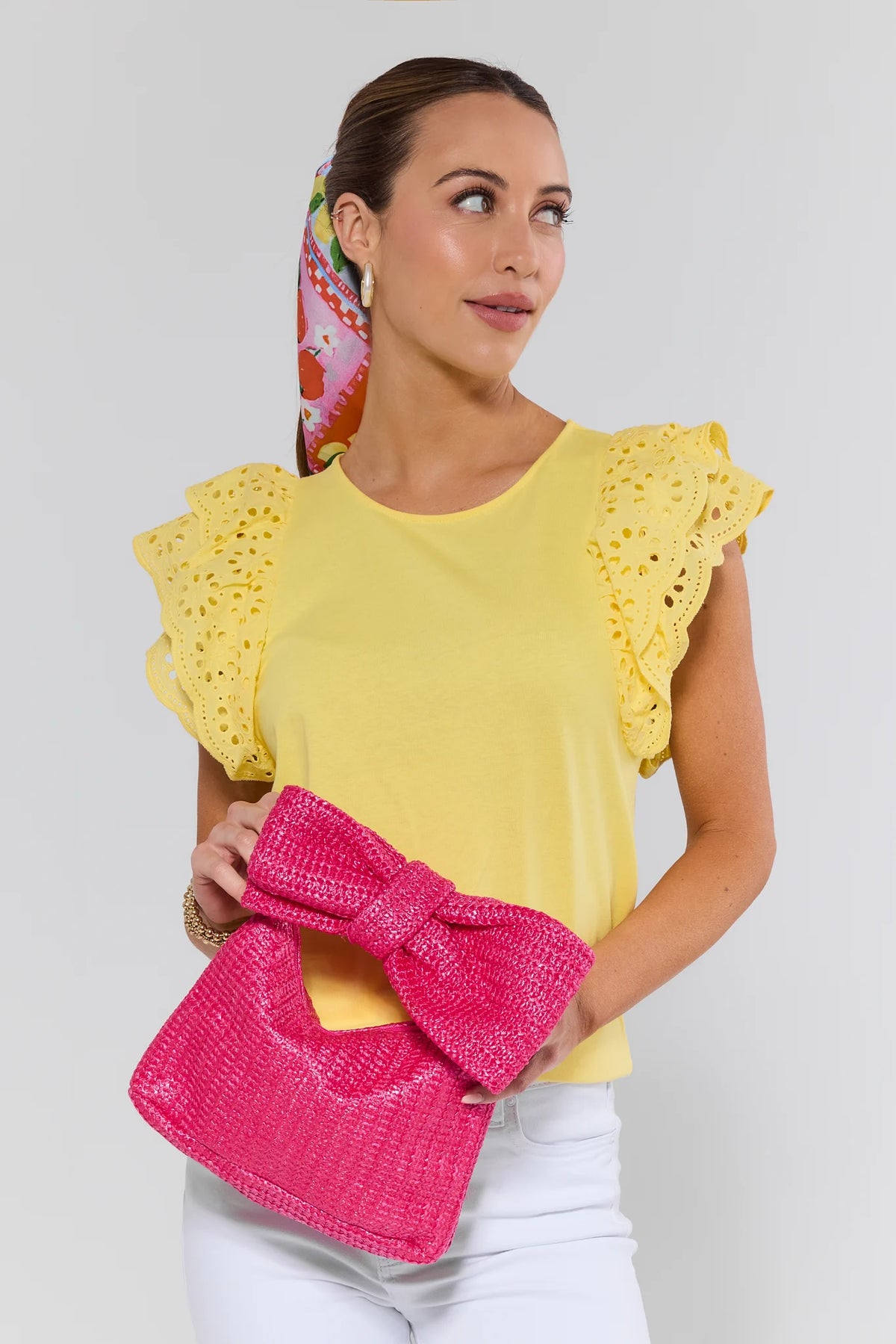 Woman in yellow ruffle top holding pink raffia bow clutch - Styled Look | Avara