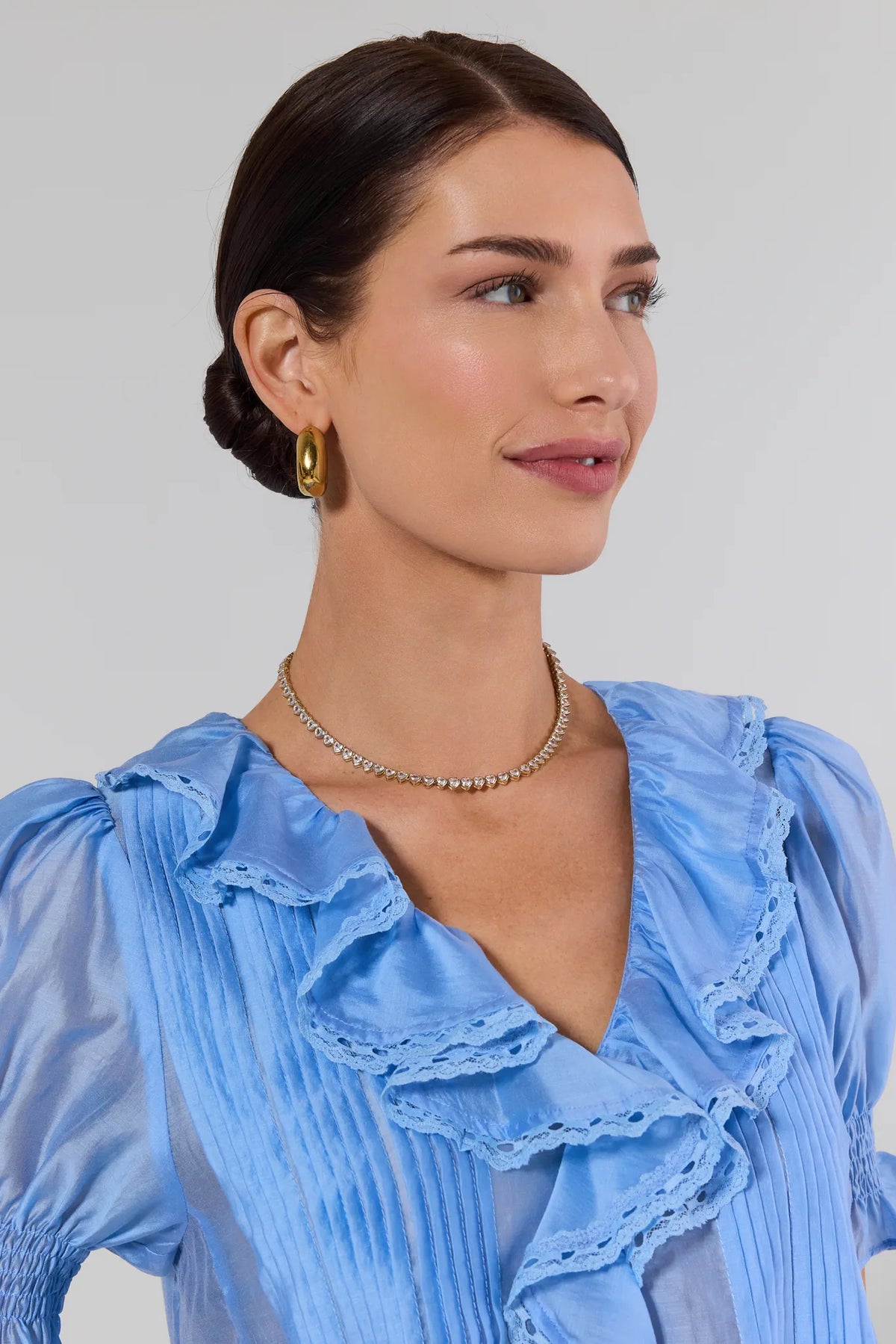 Gold heart tennis necklace worn on model in blue ruffled blouse - On Model | Avara
