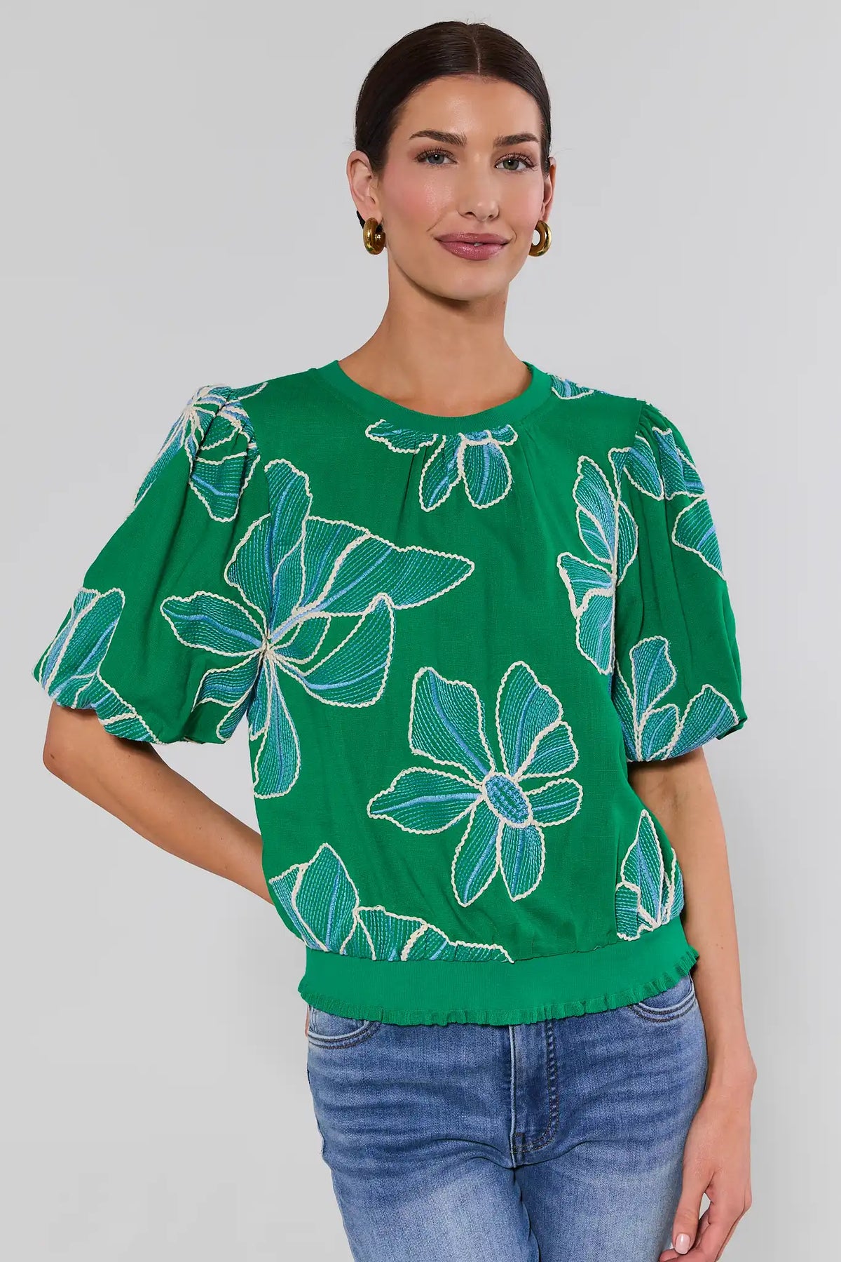 Woman wearing a green blouse with blue floral patterns on a plain background