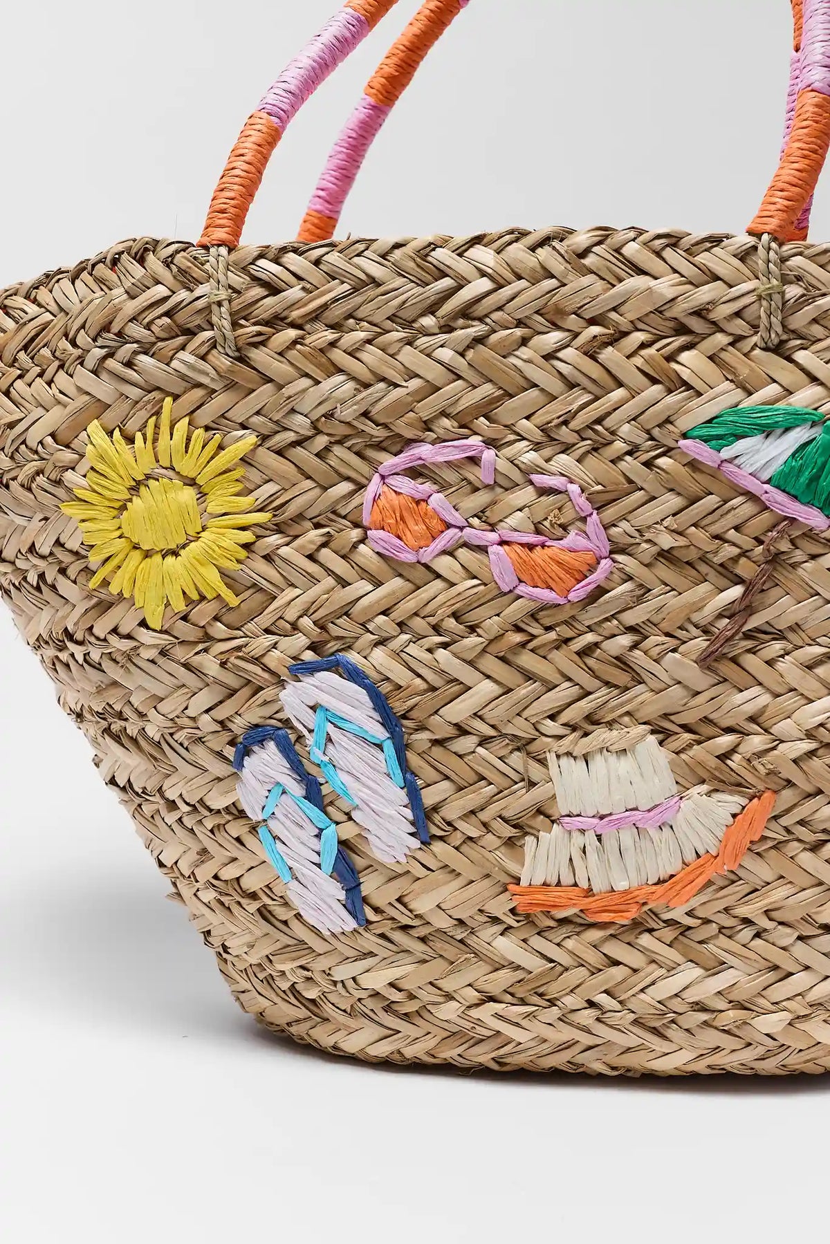 Close-up of woven raffia tote with sun, sunglasses, flip flop and hat embroidery detail | Avara