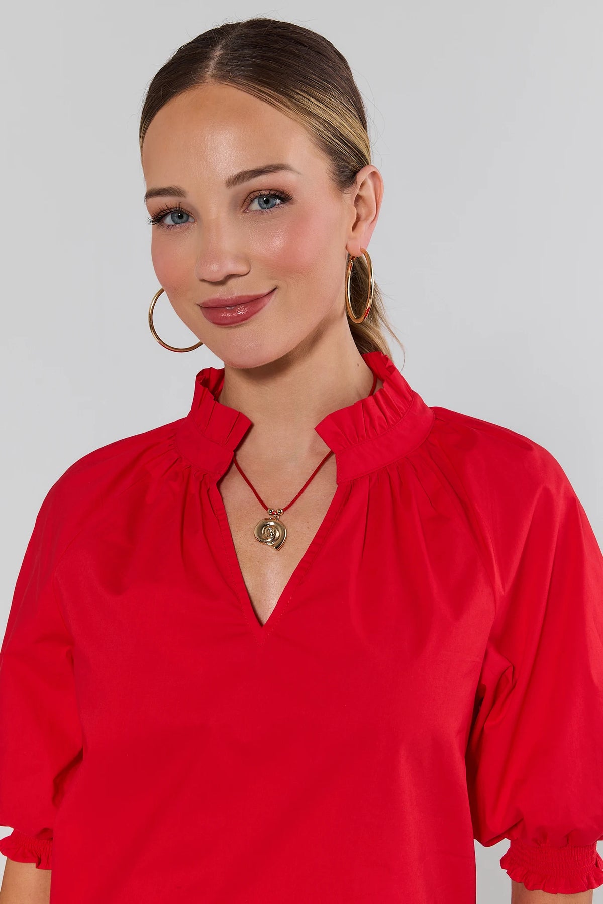 Woman wearing red cord shell necklace with gold spiral pendant styled with red ruffle blouse - On Model | Avara