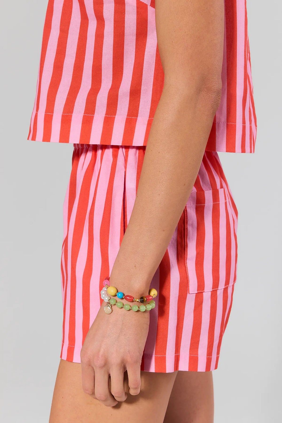 Person wearing a red and white striped outfit with colorful bracelets on a gray background