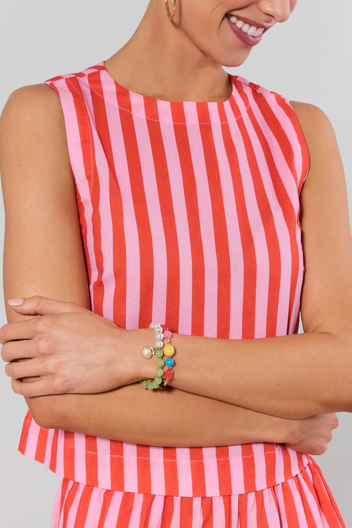 Person wearing a red and pink striped dress and bracelets with a plain background