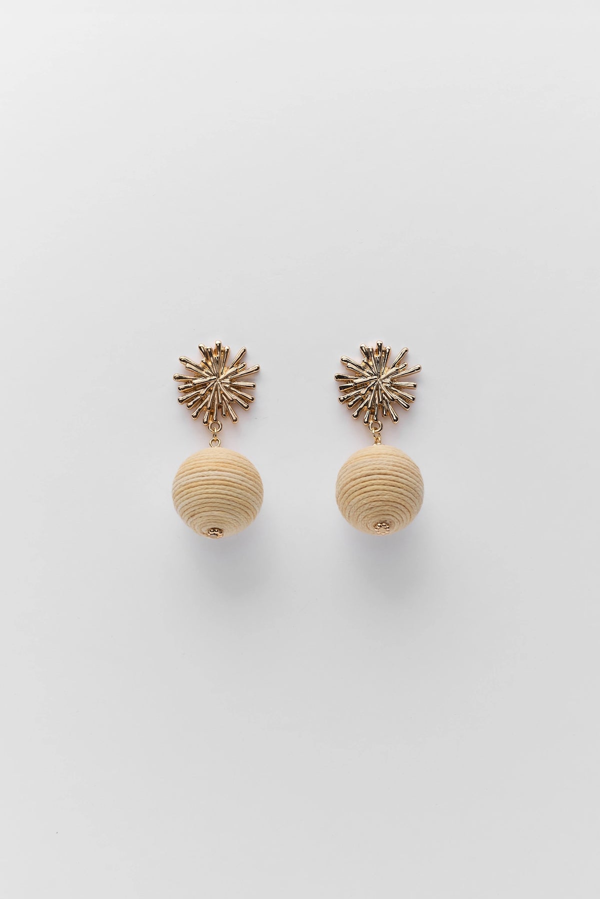 Pair of earrings with beige spherical beads and starburst tops on a light gray background