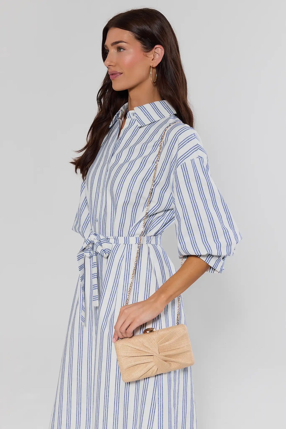 Woman in Blue Striped Midi Dress Wearing Tan Textured Knot Clutch as Crossbody - Side Styled Look | Avara