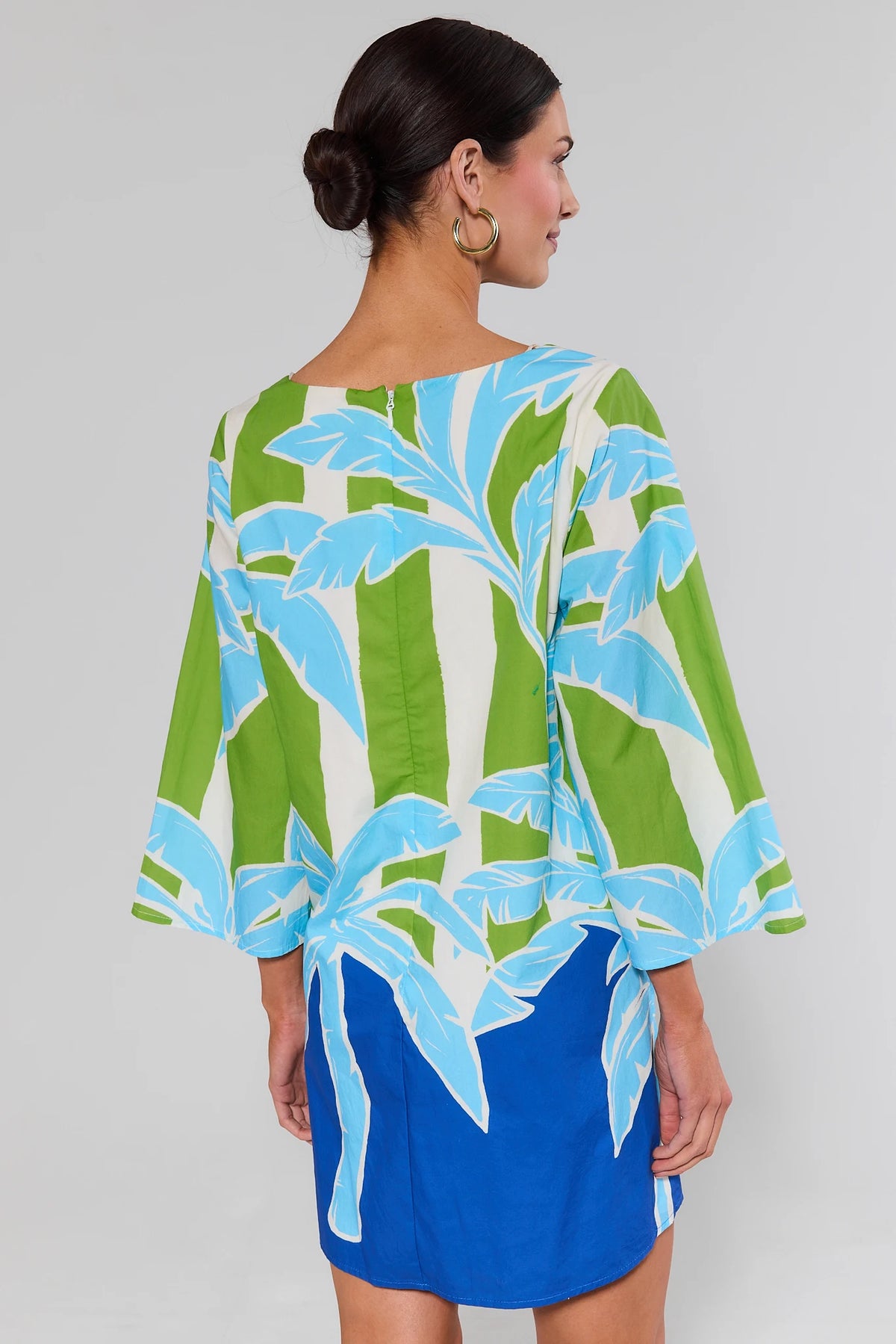 Woman standing wearing a colorful dress with leaf pattern on a plain background