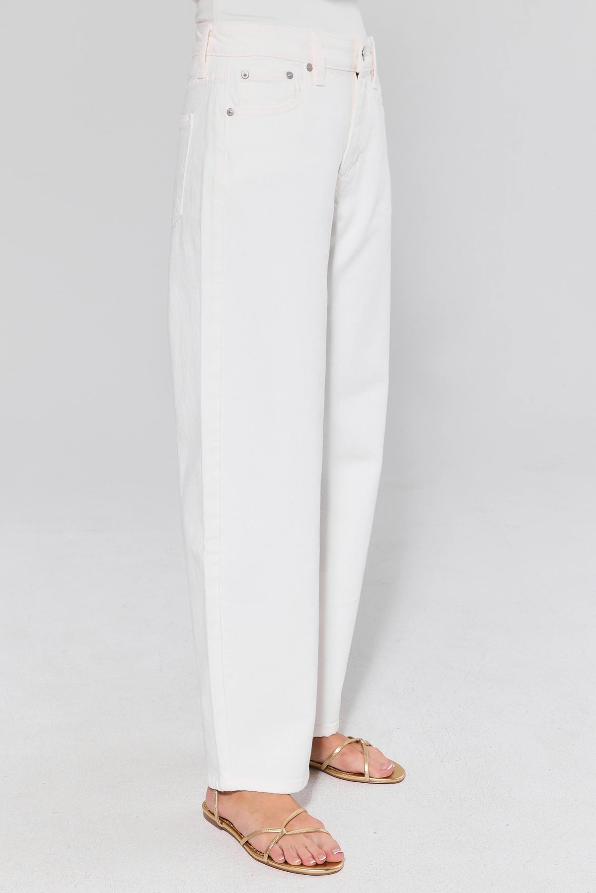 White barrel leg jeans on model with gold sandals, side profile showing curved silhouette | Avara