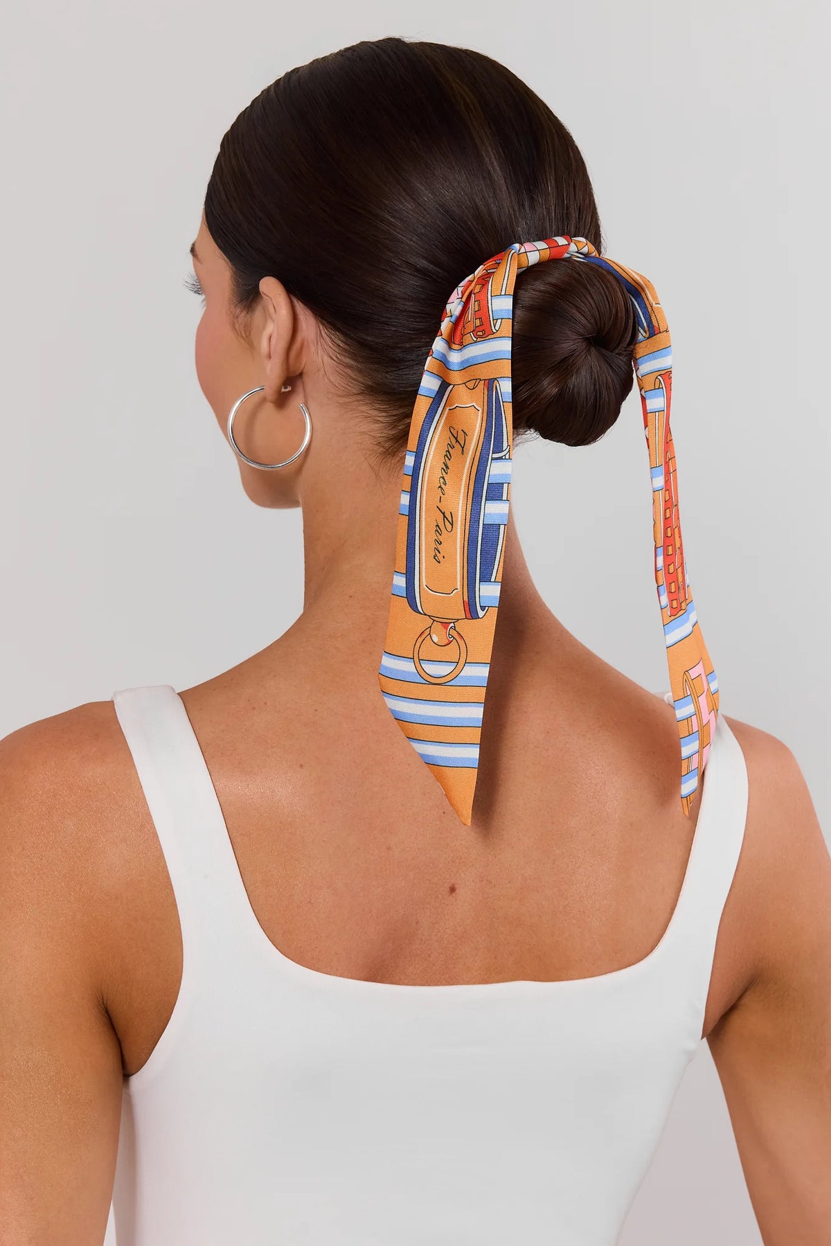 Woman styling orange multi-print skinny scarf tied in hair bun - On Model Back View | Avara