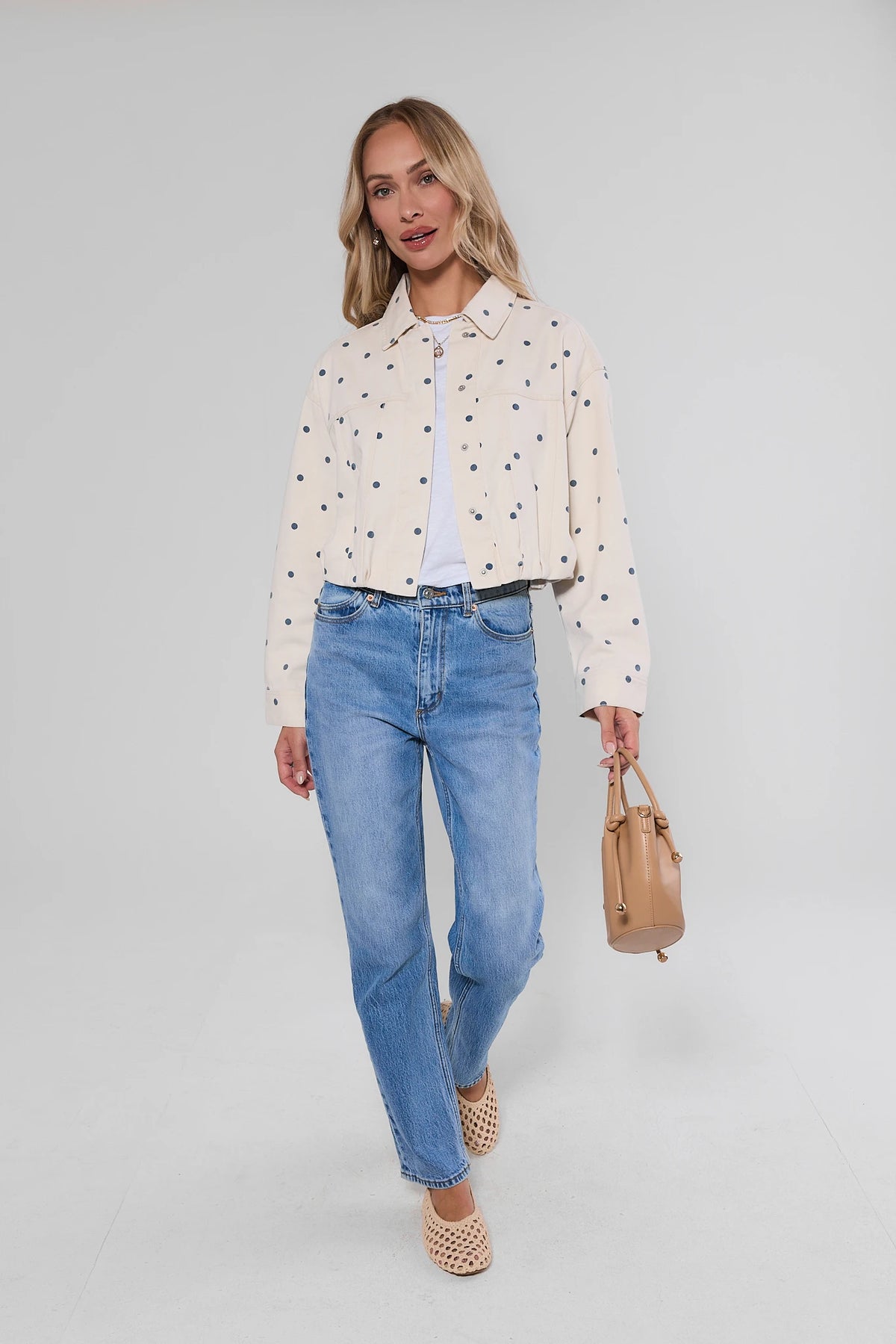 White Polka Dot Cropped Denim Jacket full-length styled look with blue jeans and tan handbag | Avara