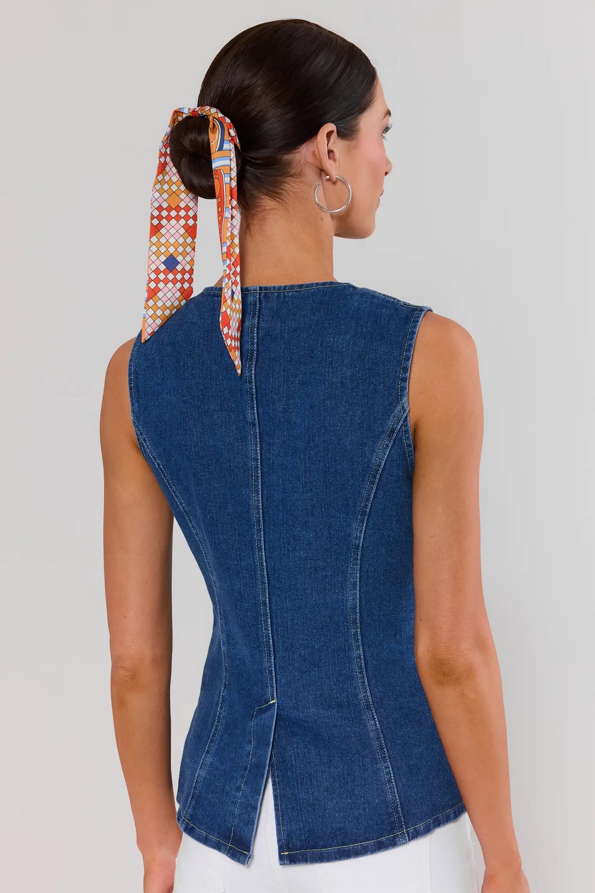 Woman standing wearing a blue denim sleeveless top with a colorful headscarf, on a plain background