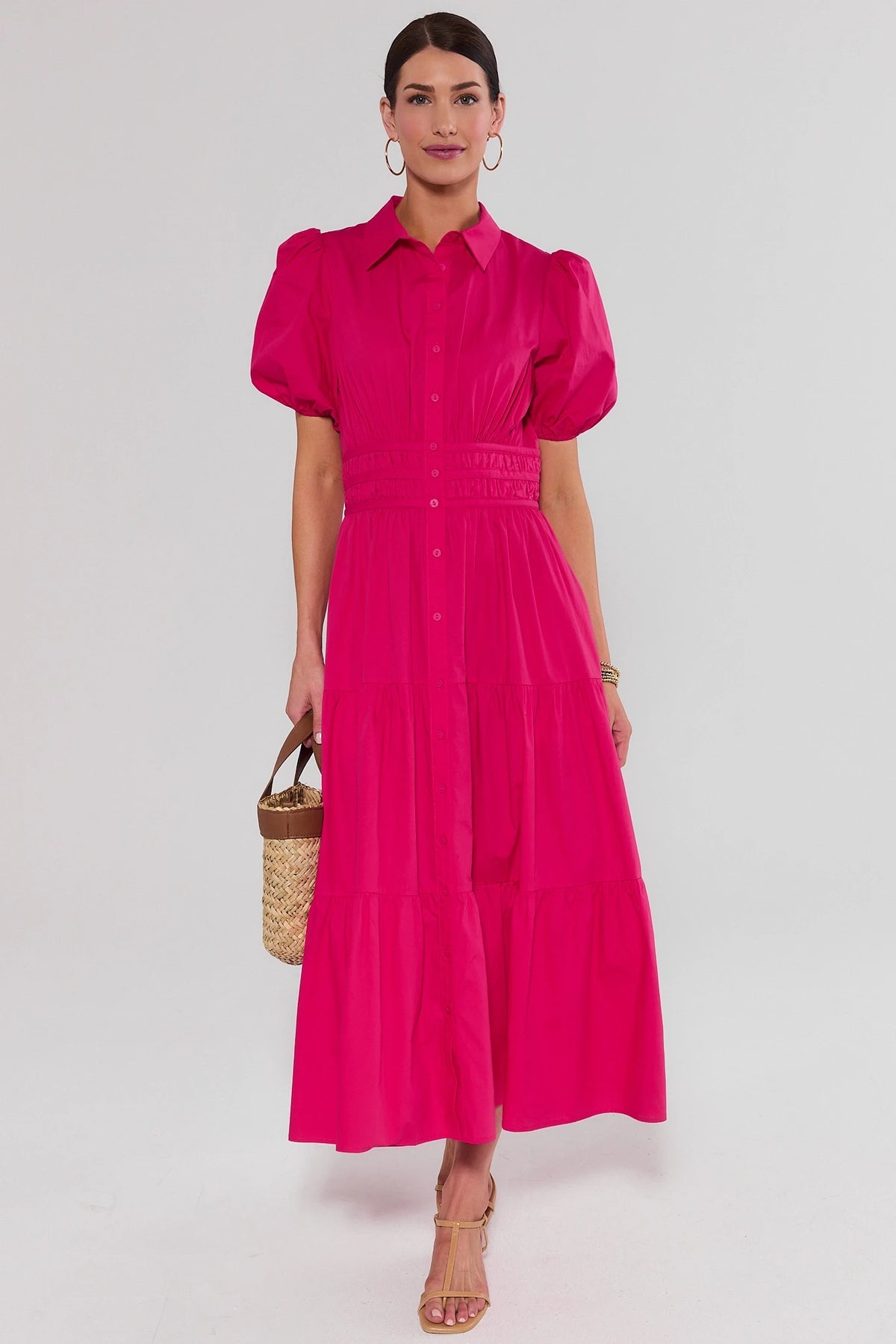 Woman standing wearing a bright pink dress with puff sleeves against a light gray background