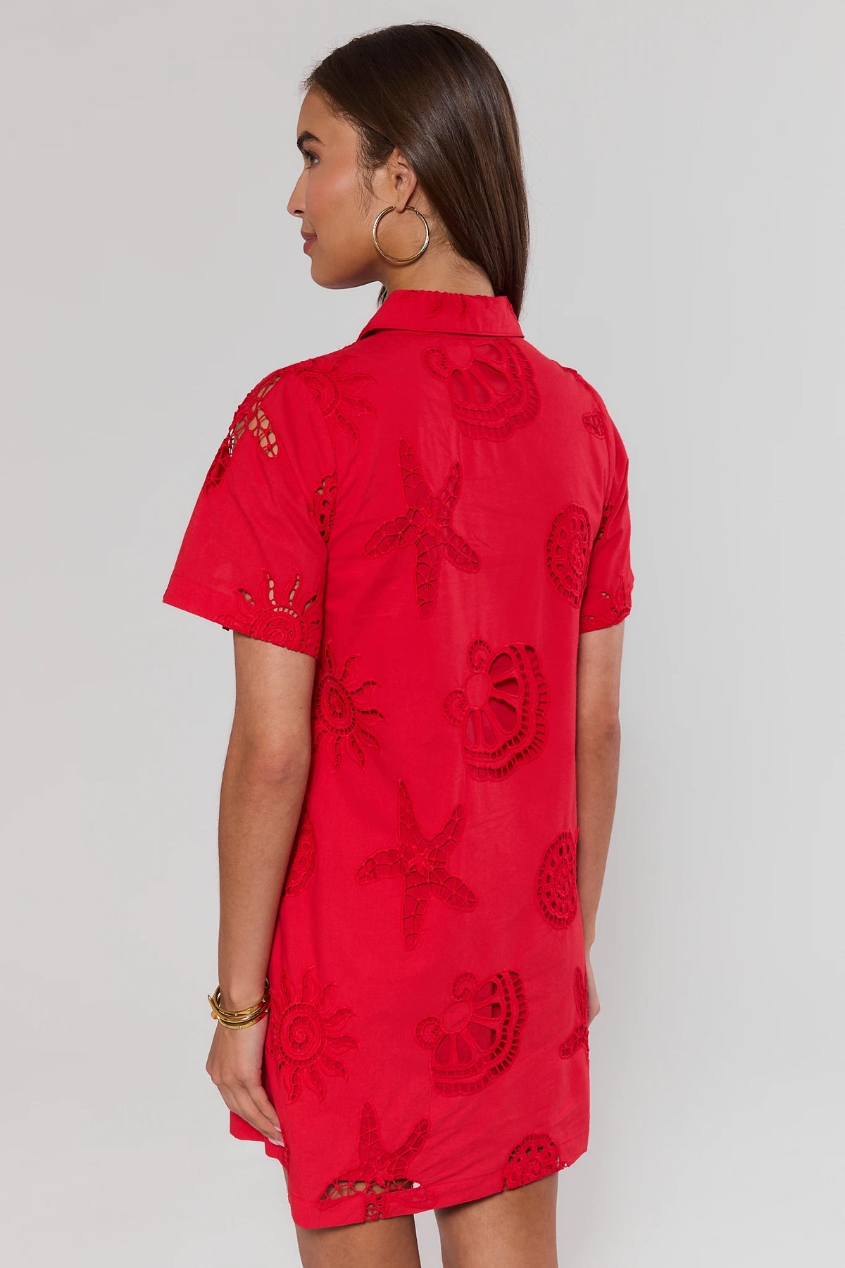 Woman wearing a red dress with floral patterns on a plain background standing