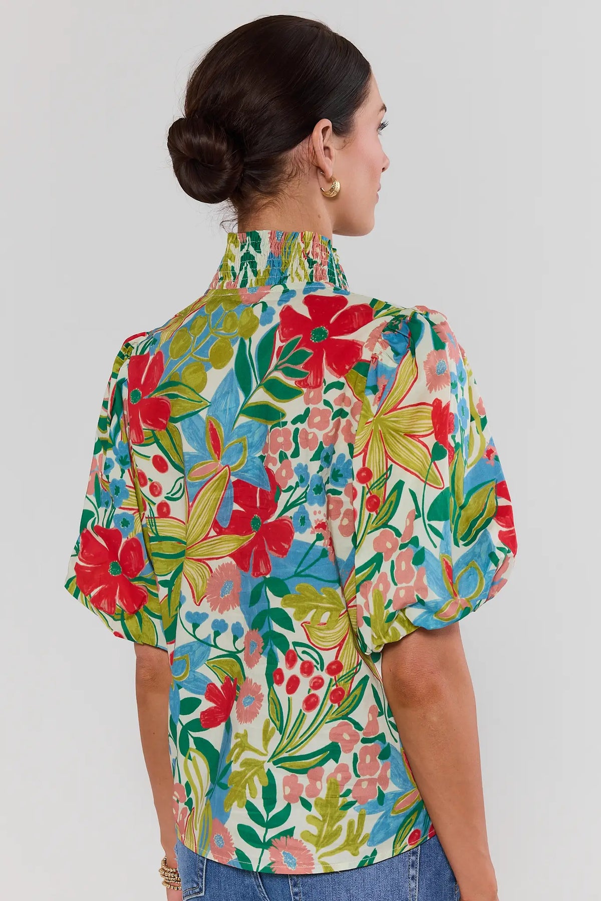 Woman standing wearing a colorful floral blouse against a plain background