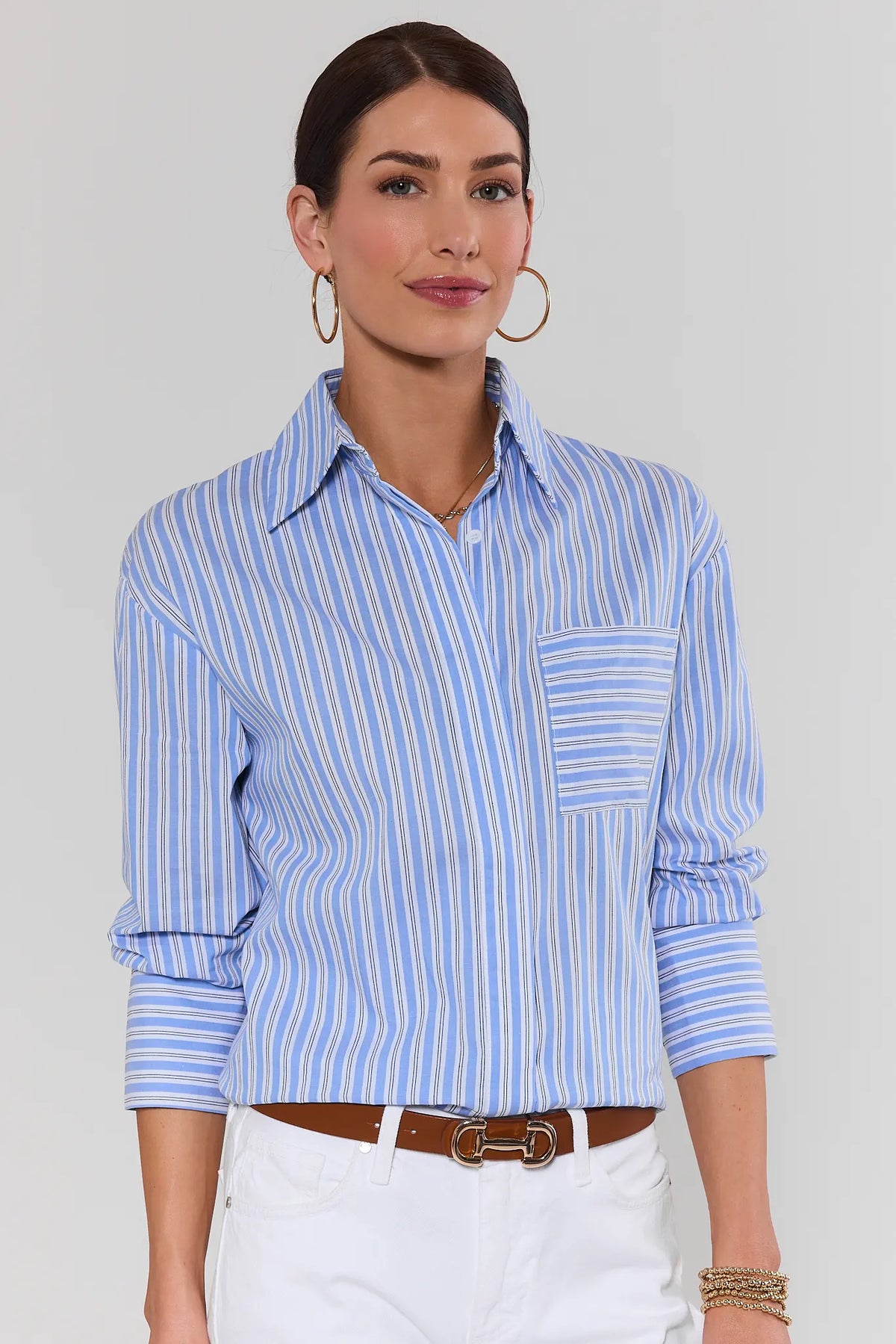 Woman wearing light blue striped button up shirt tucked into white jeans with brown belt | Avara