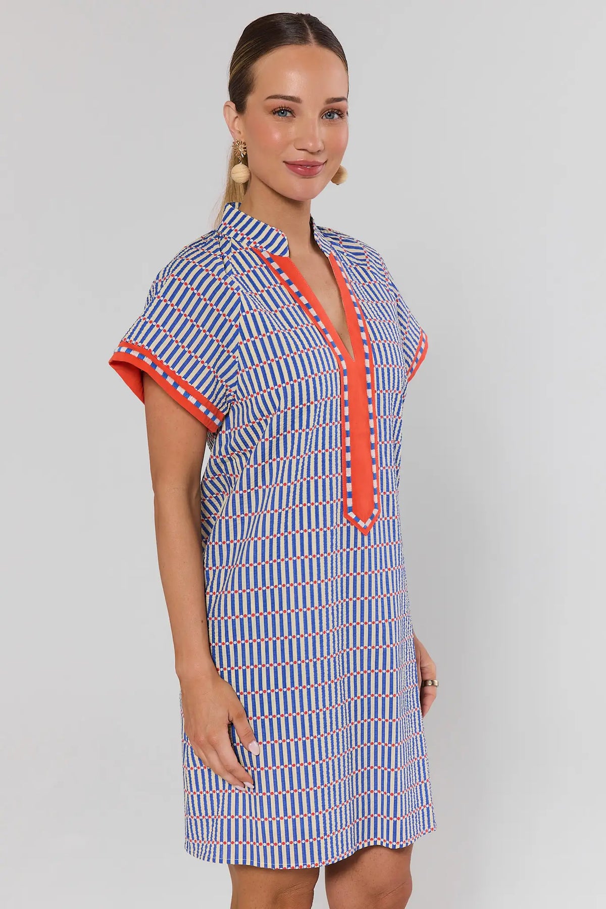 Woman wearing a blue striped seersucker shift dress with orange V-neckline trim, angled side view | Avara
