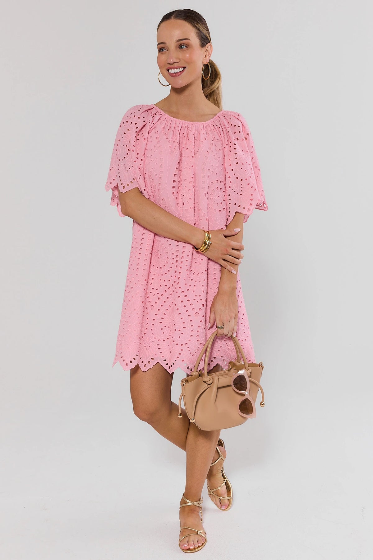 Woman wearing pink eyelet tunic dress styled with gold strappy sandals and beige handbag, full-length | Avara