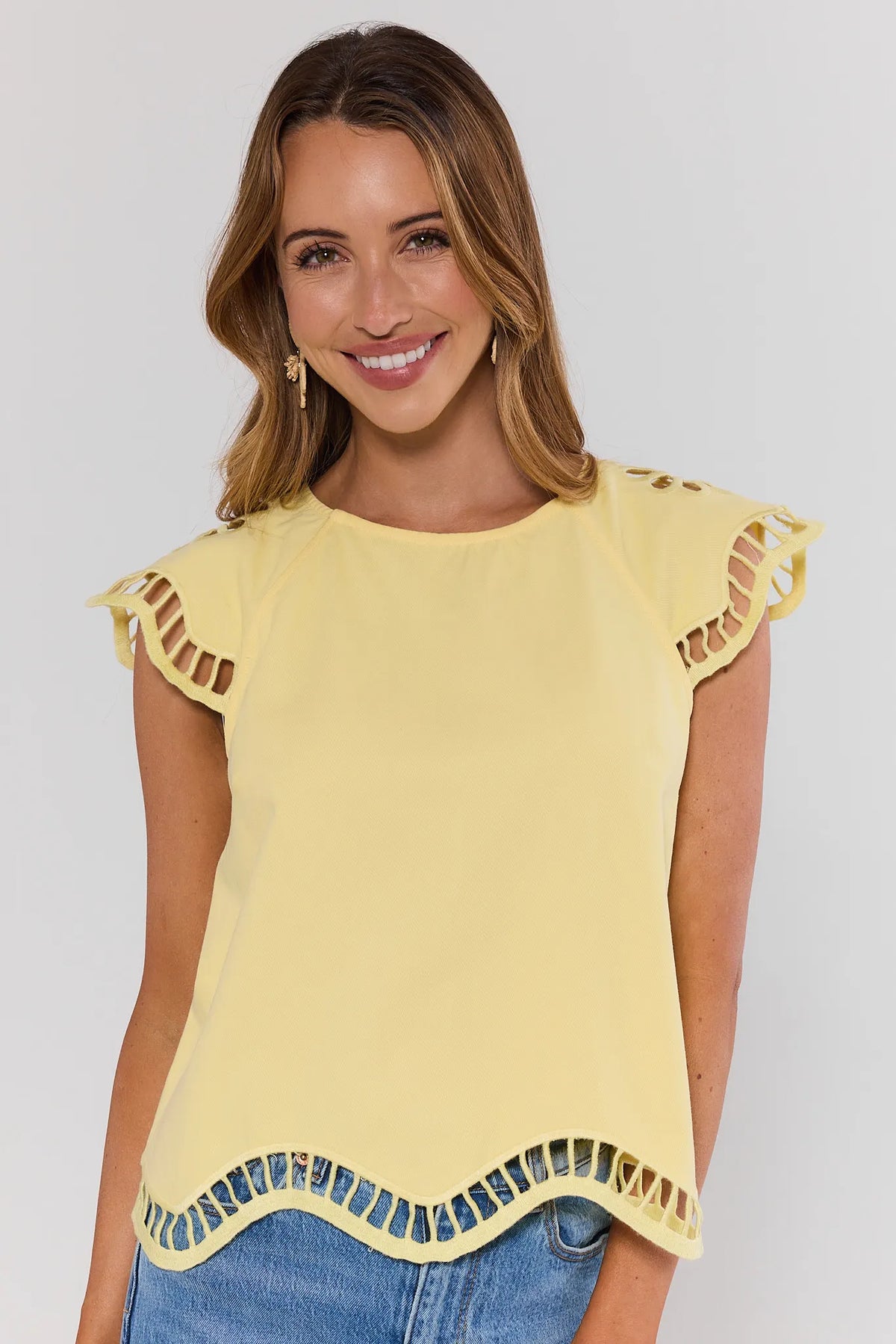 Woman wearing a yellow top with ruffled sleeves and hemline against a plain background