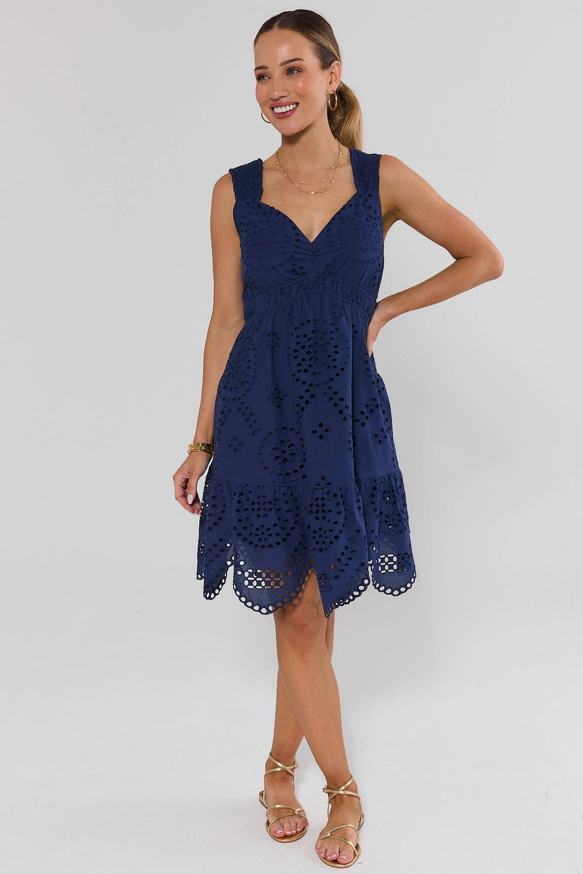 Woman standing wearing a navy blue dress with lace details on a white background