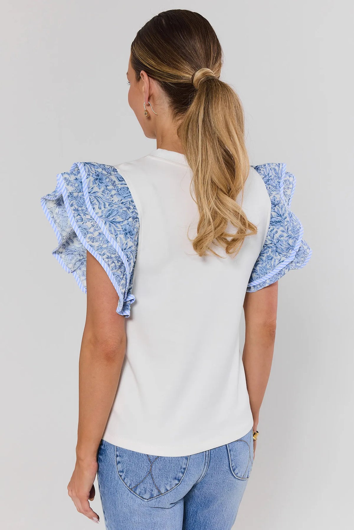 Woman wearing a white top with blue patterned sleeves against a plain background standing