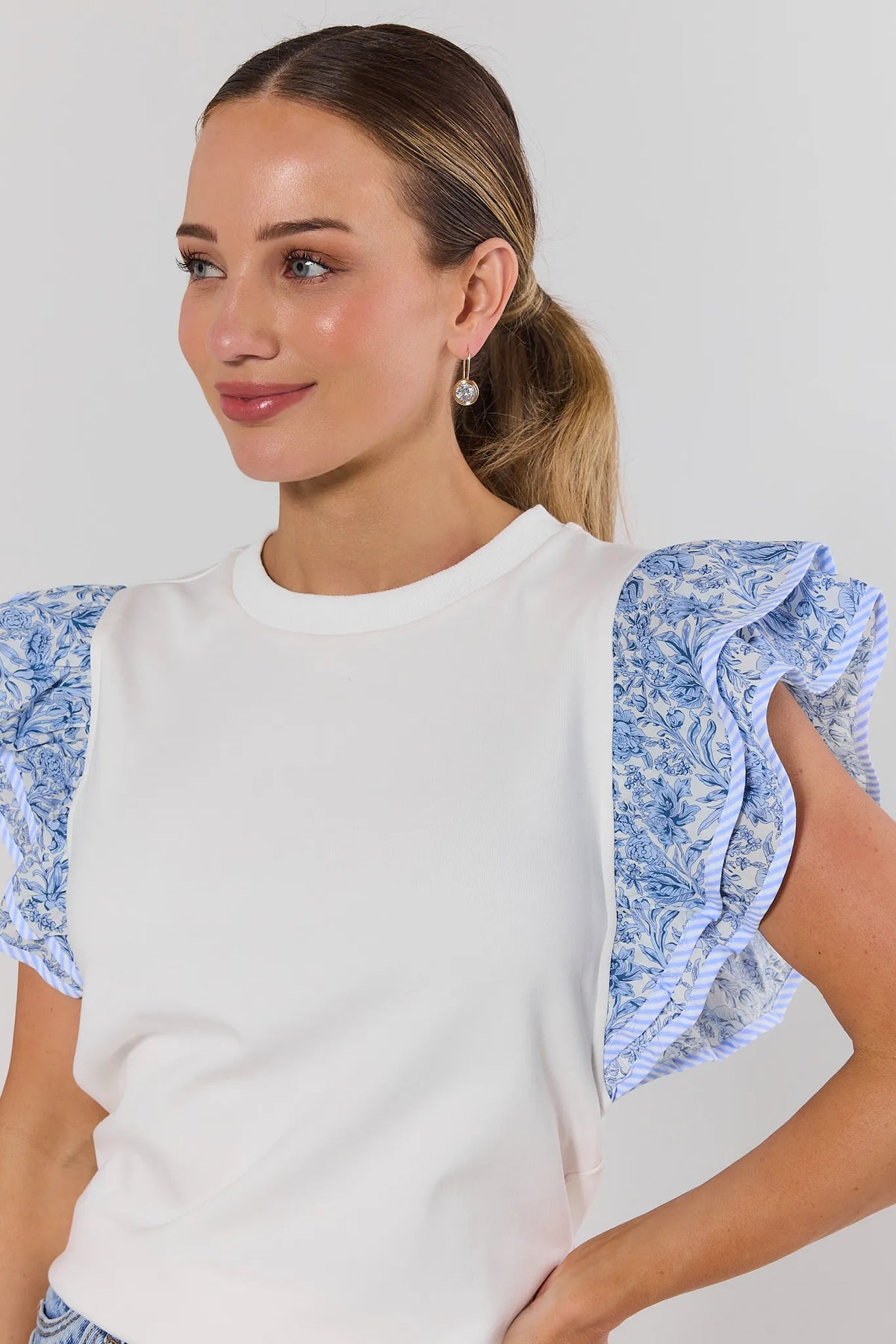close up Woman wearing a white top with blue floral sleeves against a plain background
